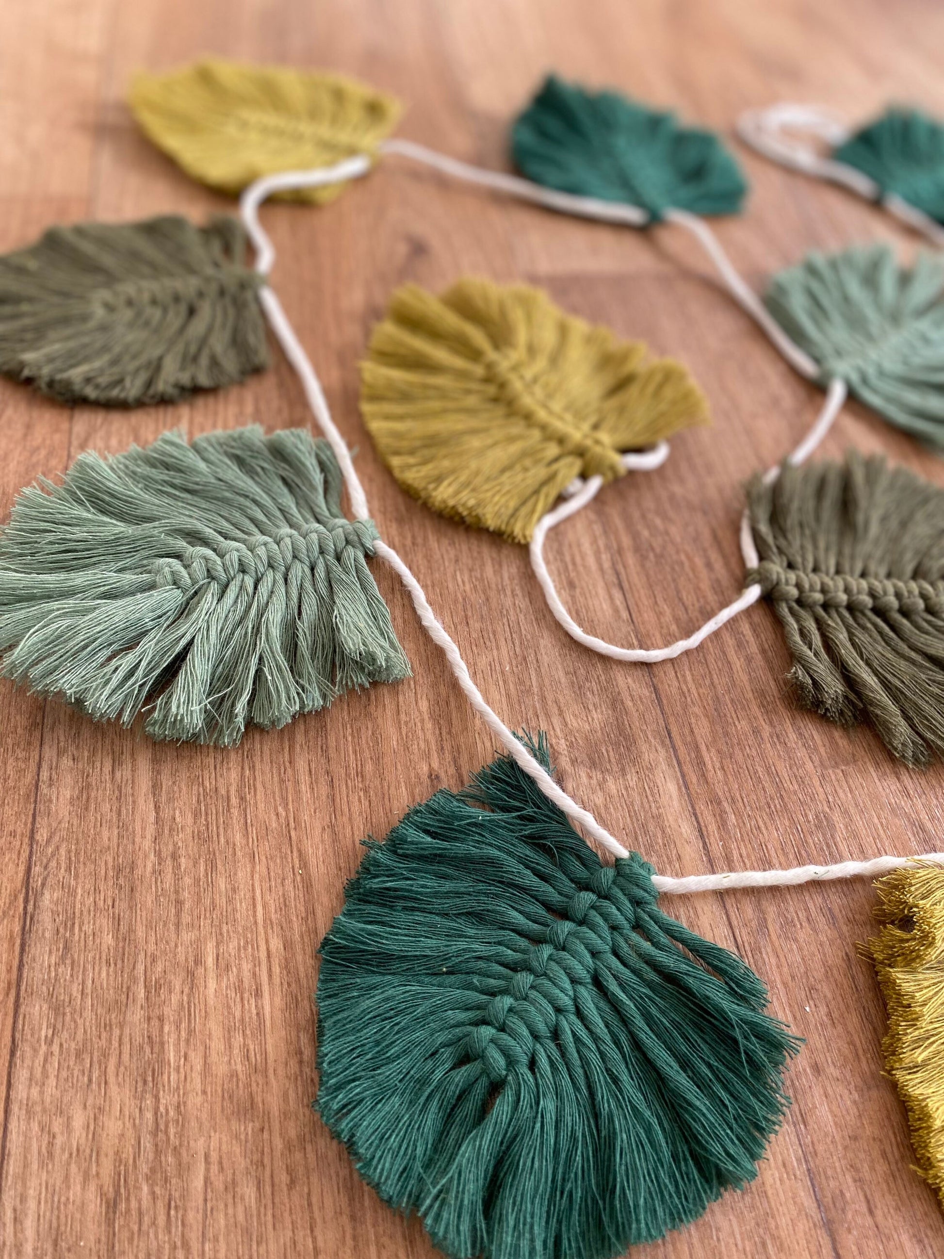A close-up image of a handmade cotton garland made of woven thread leaves in green, yellow, and olive colours, strung on a white string.