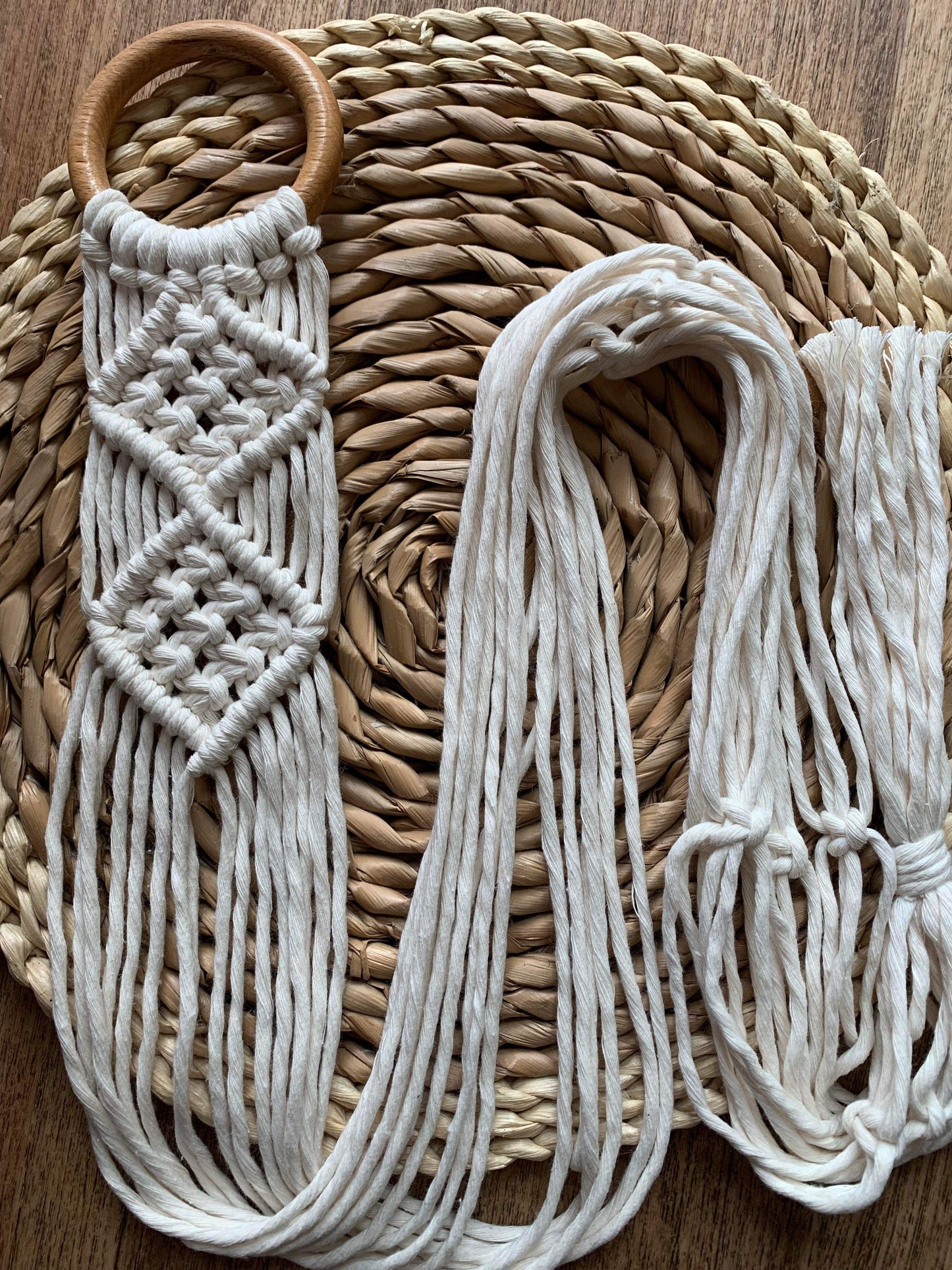 Handmade macrame banjolele wall hanger, made with natural coloured yarn on a wooden ring, laid neatly across a circular woven wicker mat.