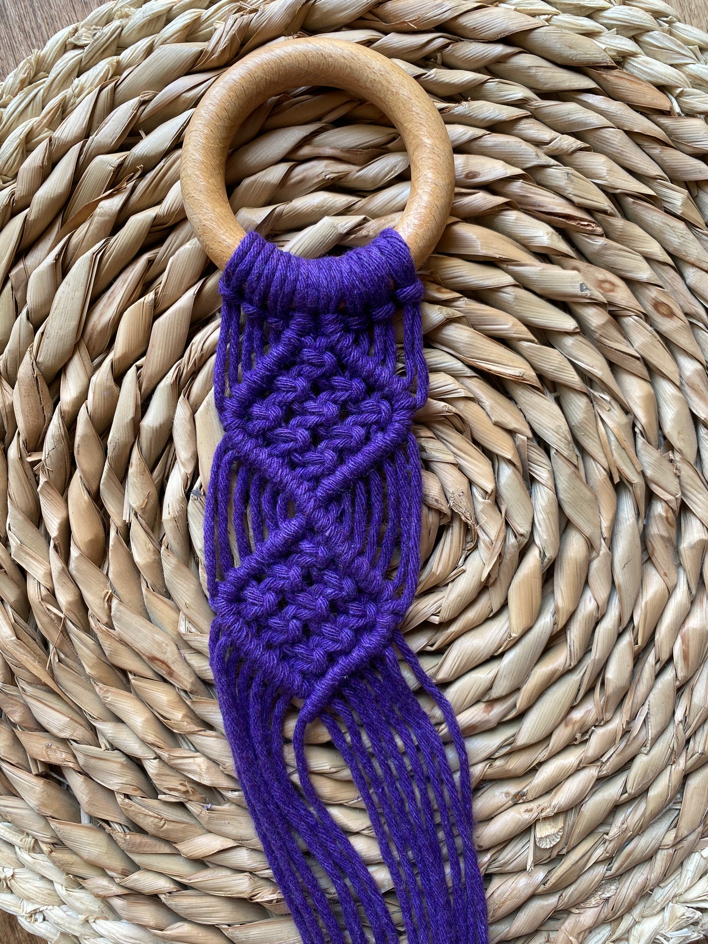 Handmade macrame banjolele instrument hanger, made with bright purple yarn in an intricate knot pattern, attached to a wooden ring.