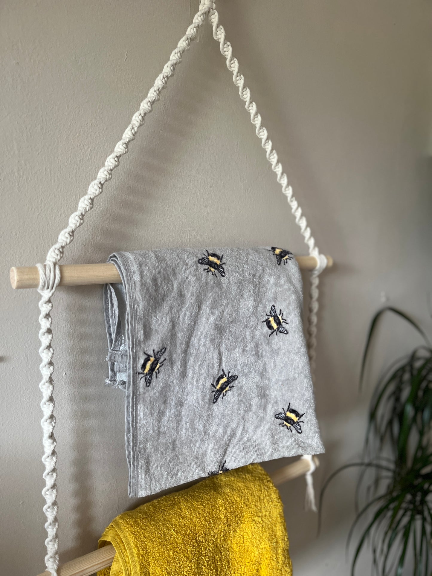 Grey towel with bee pattern hanging on a rope holder, against a neutral wall.