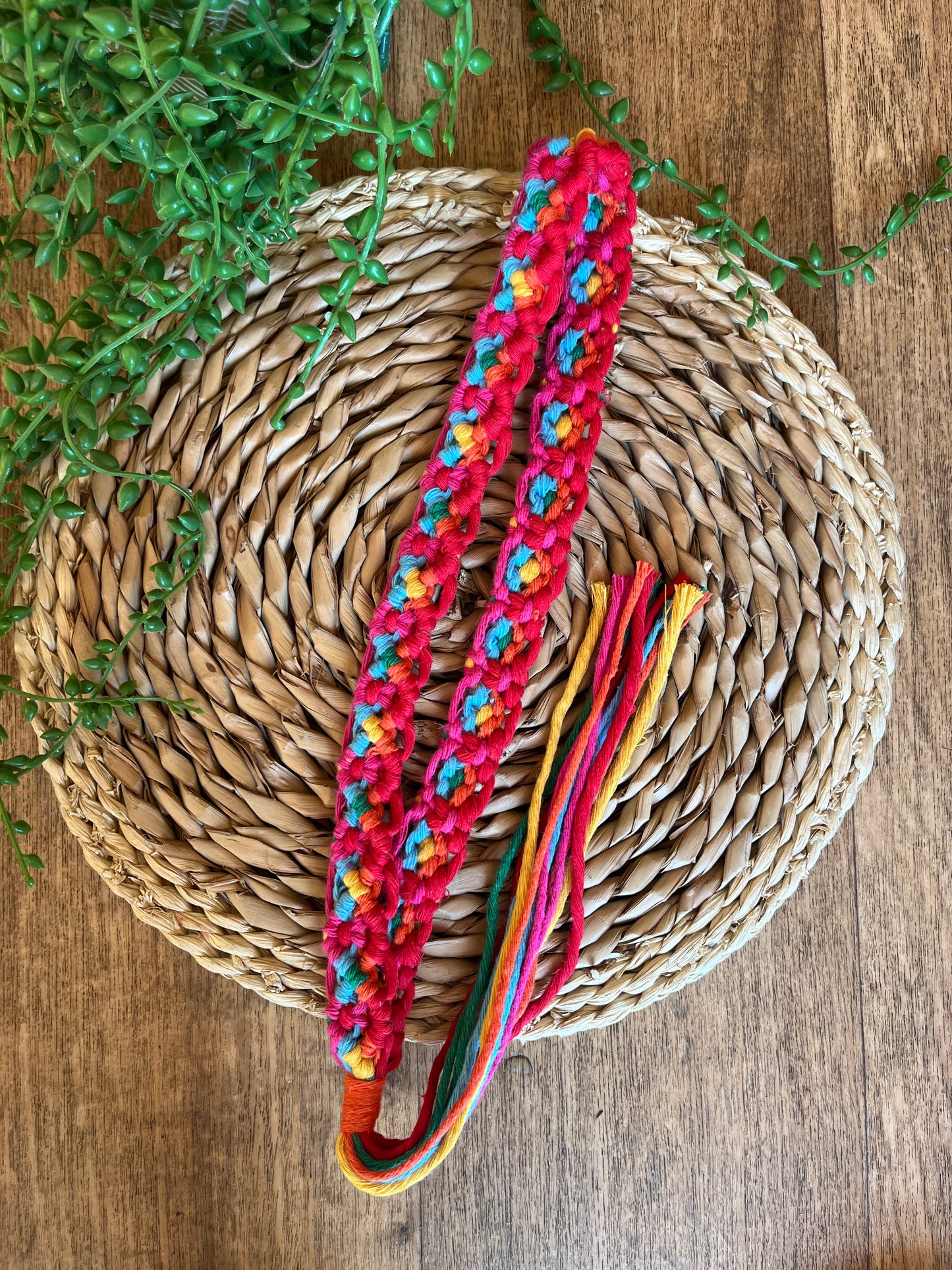 A handmade boho style macrame hat band with a long tassel. The hat band is made with an intricate knot pattern using rainbow colours of recycled cotton.