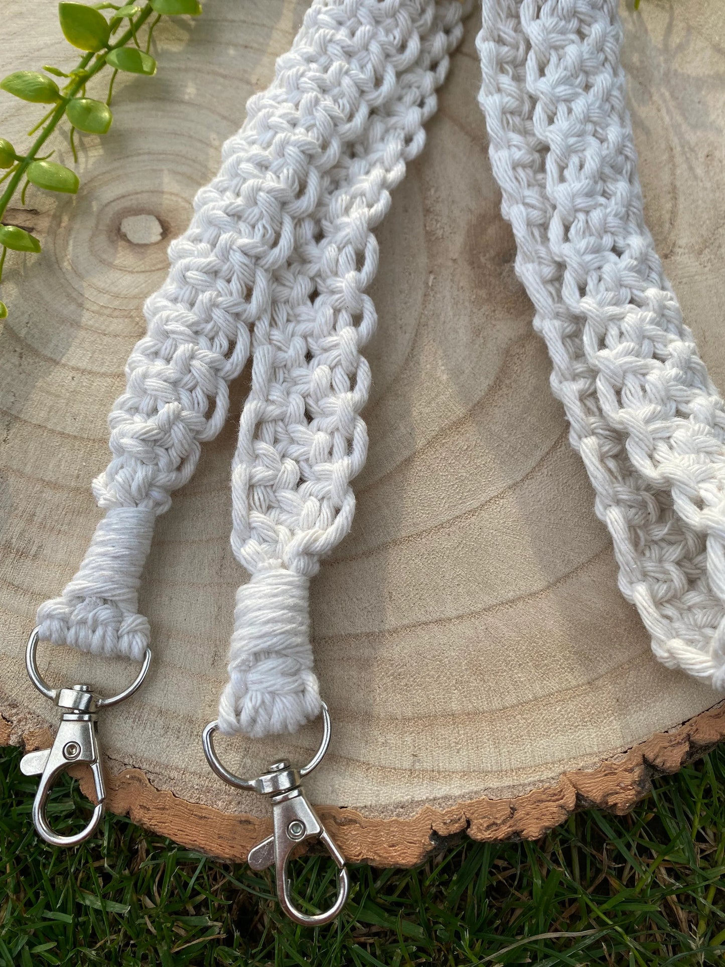 A handmade macrame knotted camera strap with metal clasps on each end, laid across a round wooden surface atop lush. green grass.