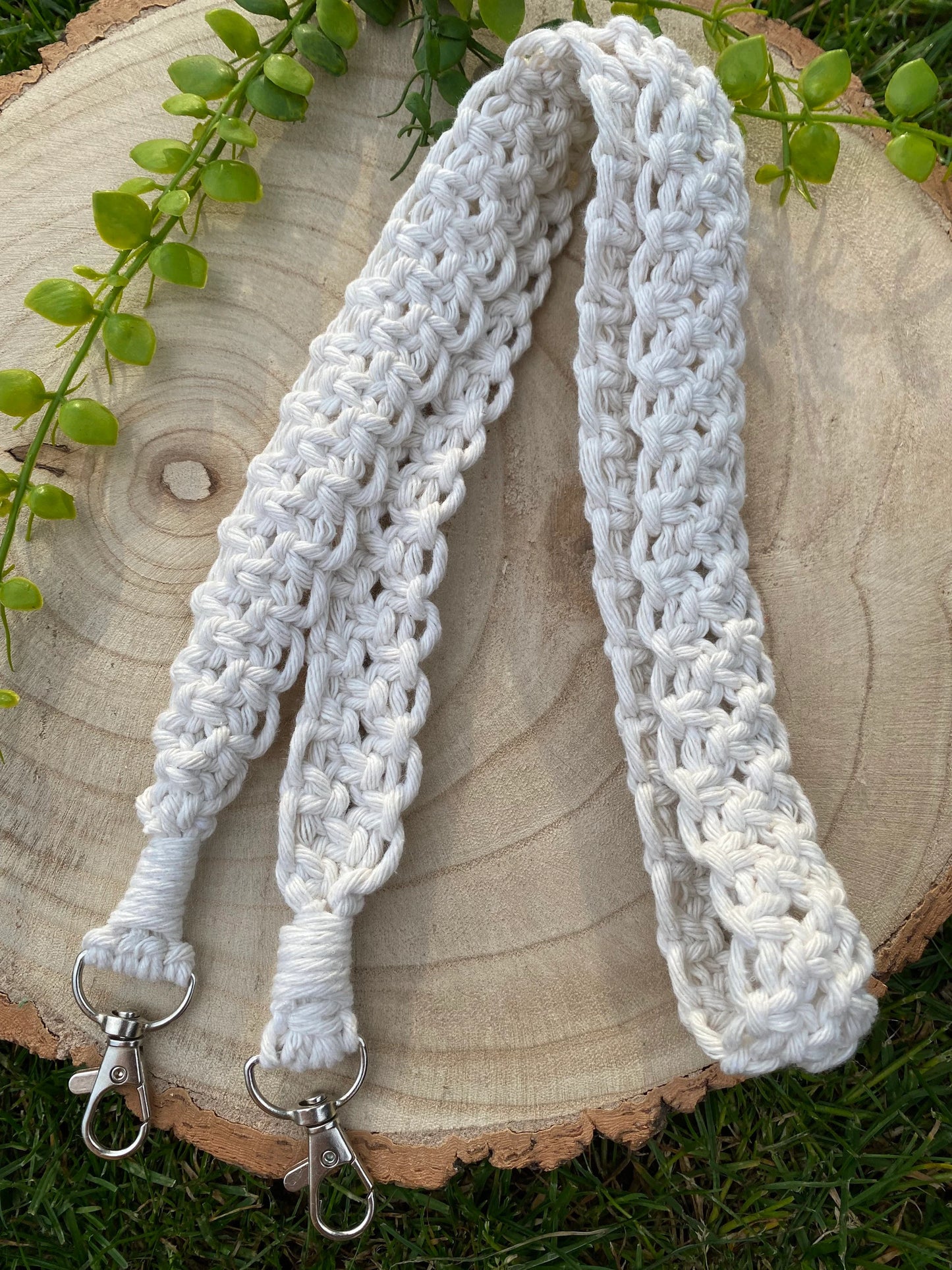 A handmade macrame knotted camera strap made with natural yarn and with metal clasps on each end.