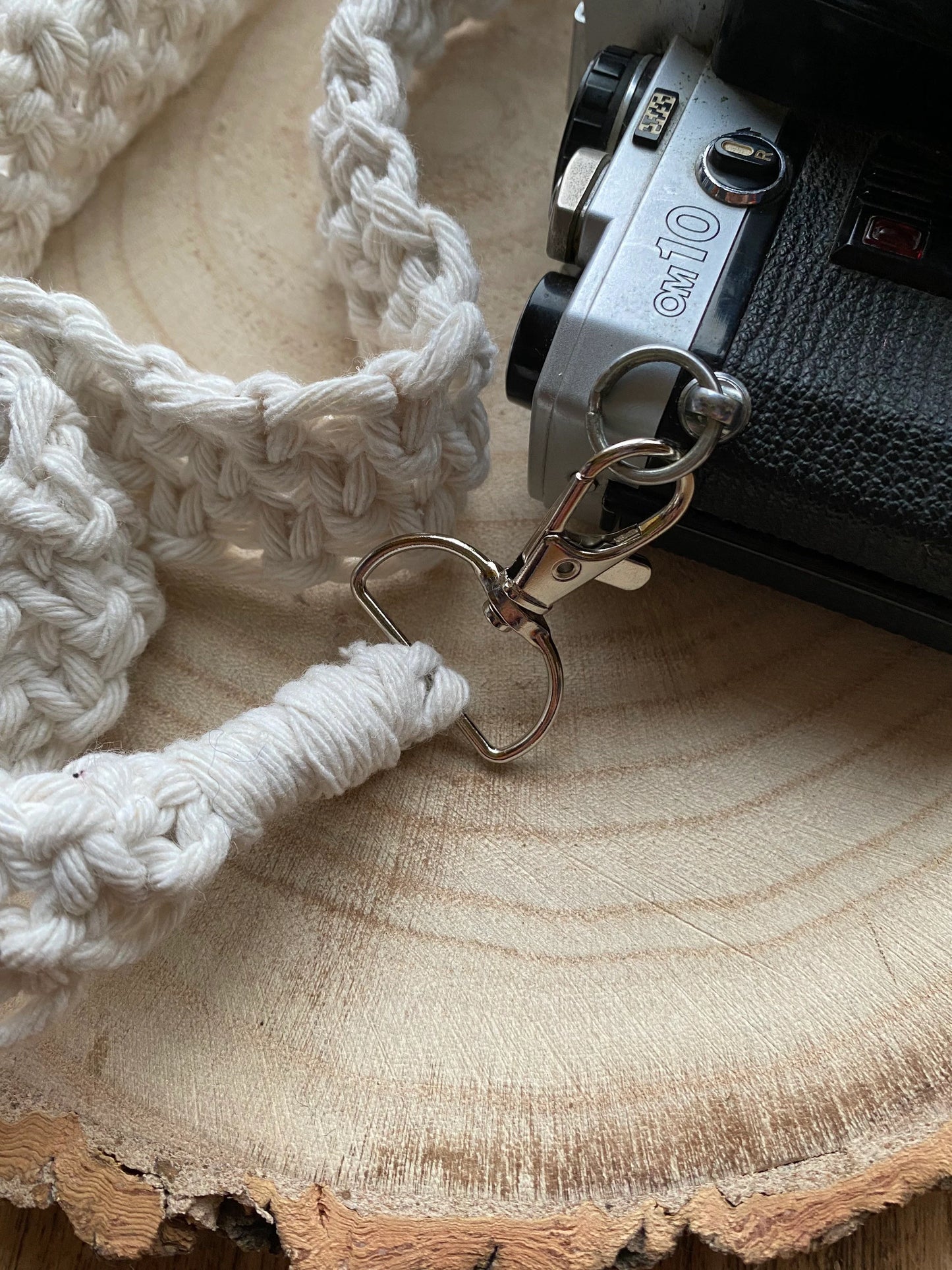 Close up of a black Olympus vintage camera on a round wooden surface, with a handmade macrame knotted camera strap attached to it with metal clasps.