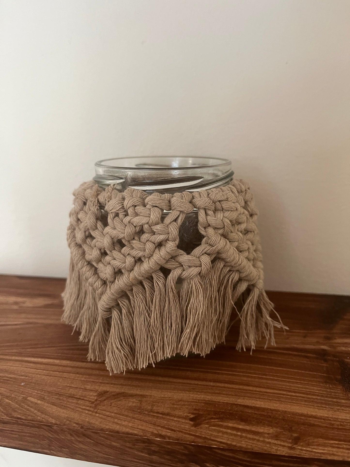 Glass jar with a macrame cover on a wooden shelf.