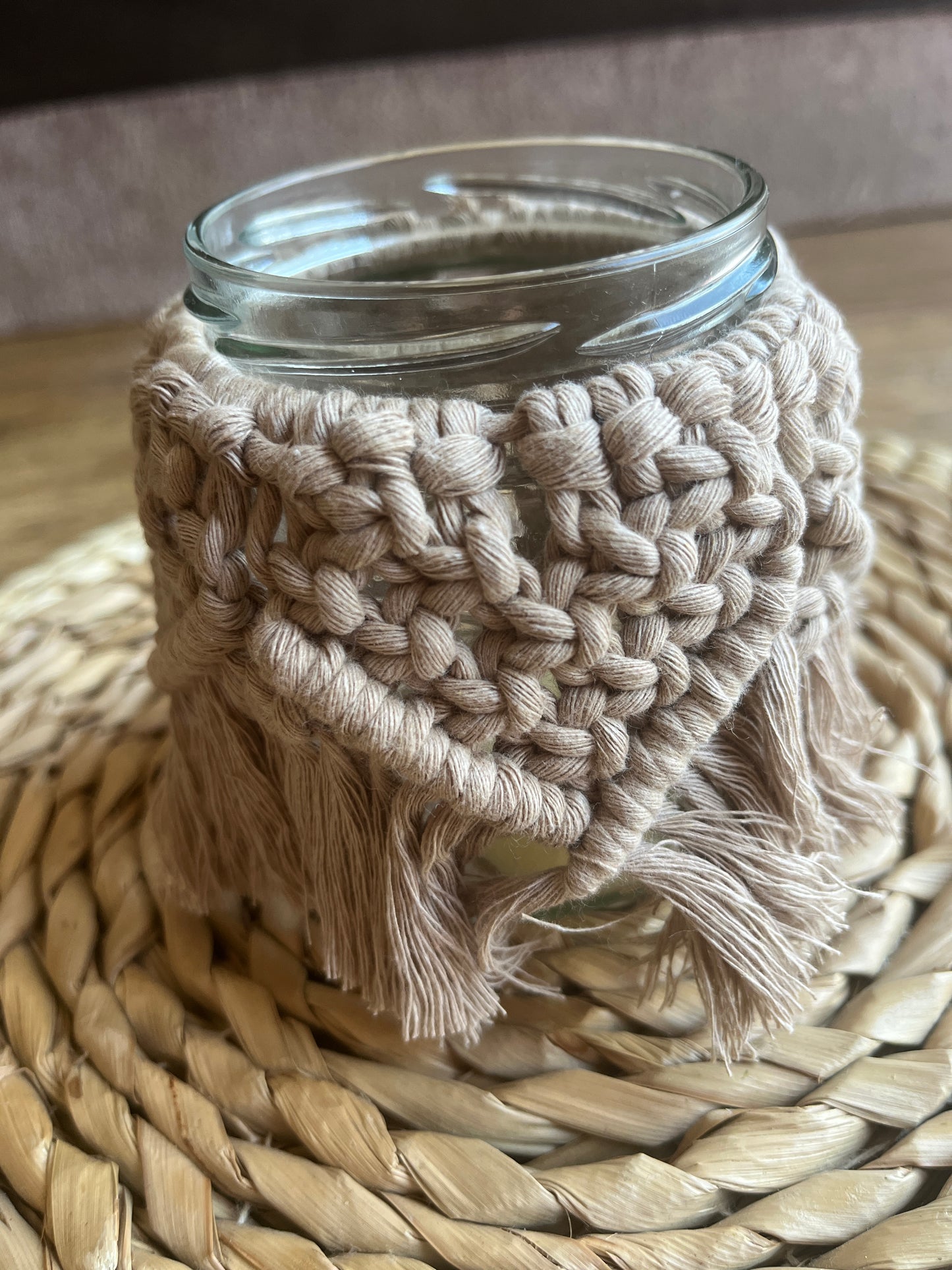 Close up of a glass jar wrapped with cotton yarn with a decorative knotted pattern placed on a wicker surface.