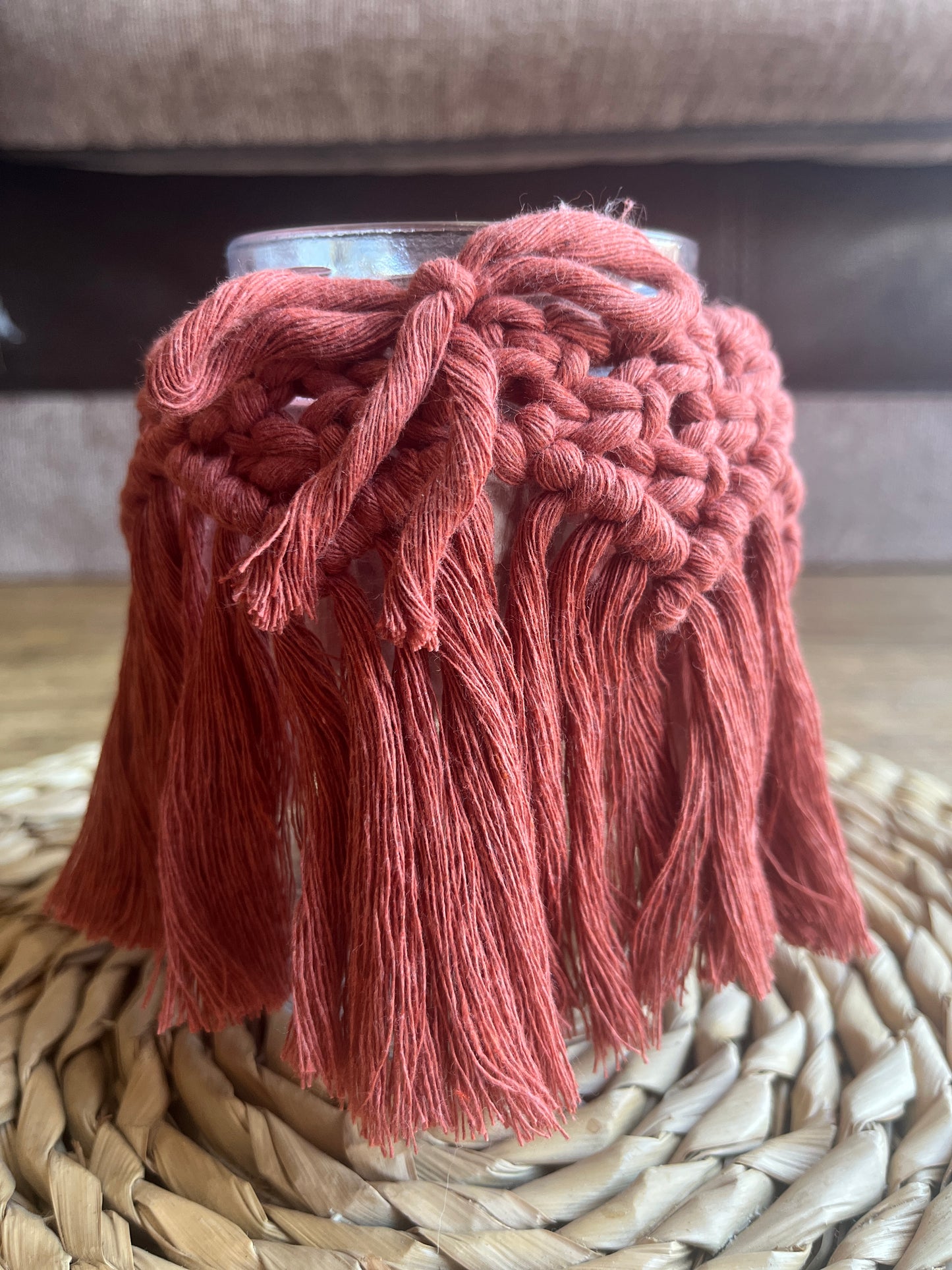 Close up of a glass jar wrapped with terracotta cotton yarn with a decorative knotted pattern and finished with a bow, on a wicker mat.