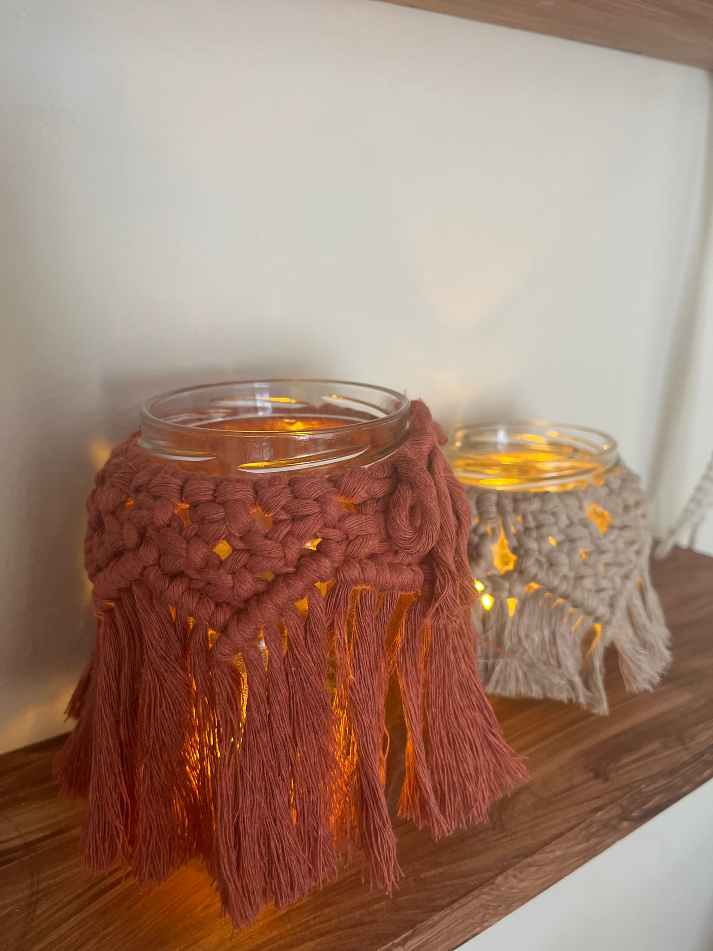 Decorative glass jars with macrame tassels and LED tealights on a wooden shelf.
