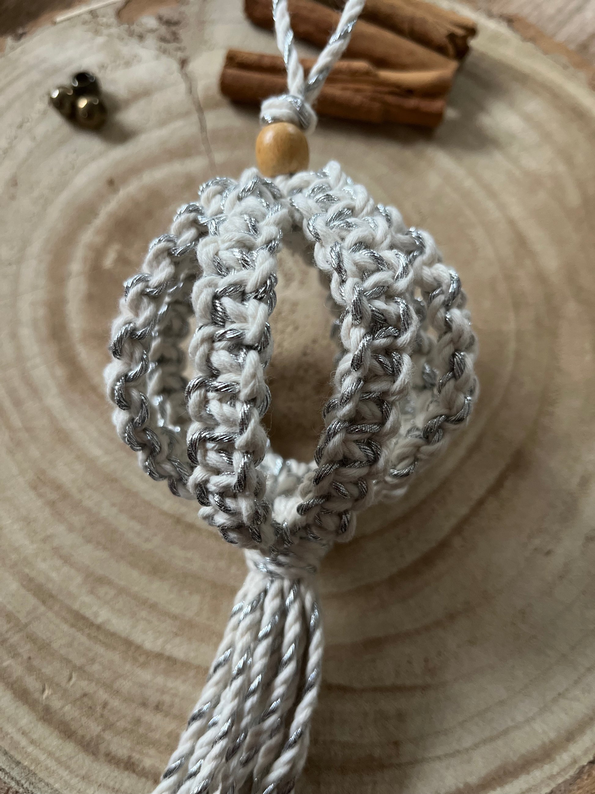 Close up of a macrame Christmas bauble made with natural cotton yarn, and finished with a small wooden bead.