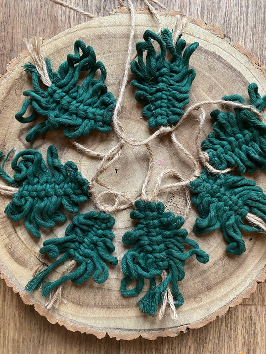 A garland of handmade macrame christmas trees, made with pine green cotton yarn on a length of jute string, displayed in a circle on a wooden board.