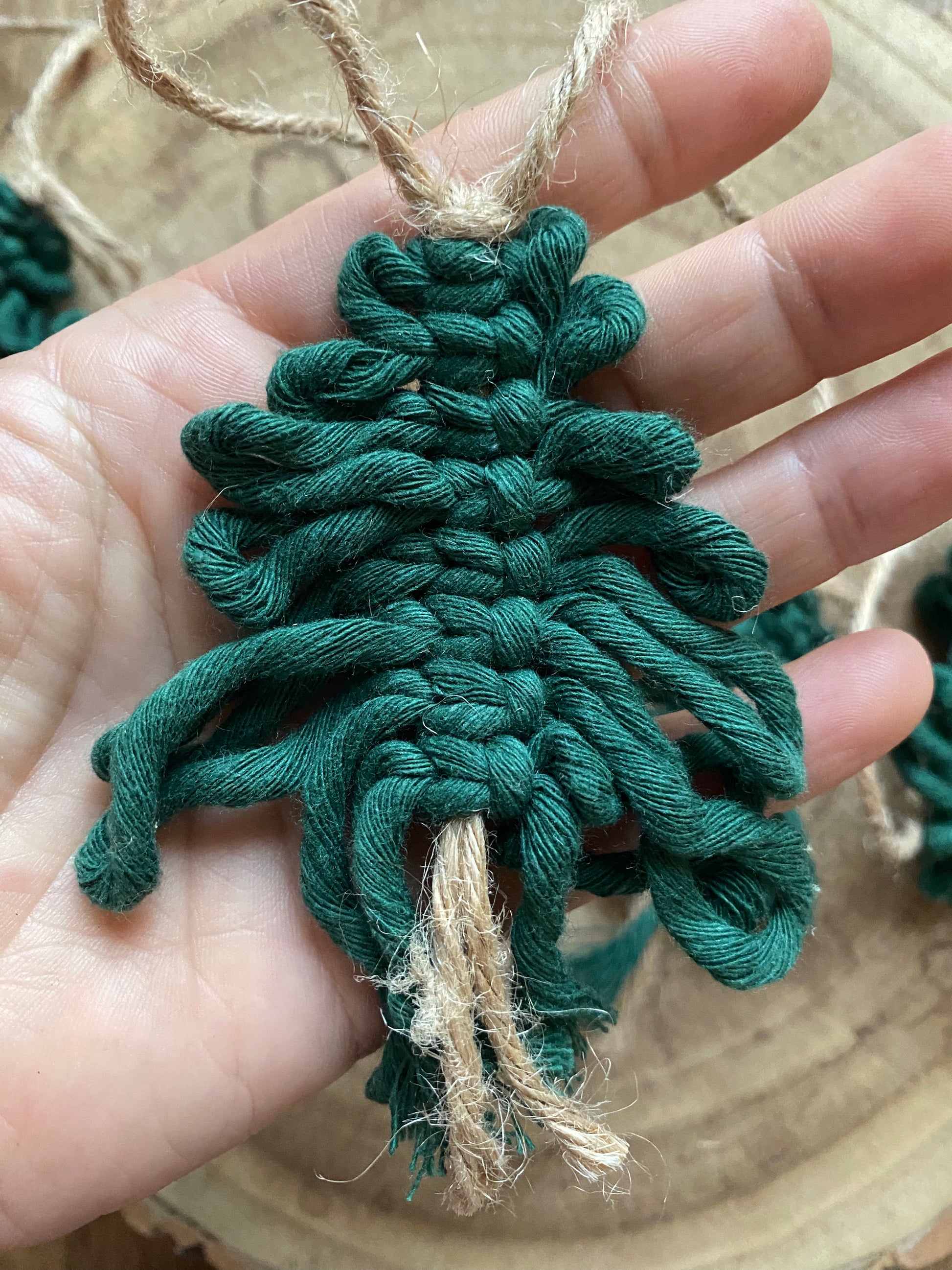 A close up image of a handmade macrame christmas tree, made with pine green cotton yarn on a length of jute string, in a persons hand.