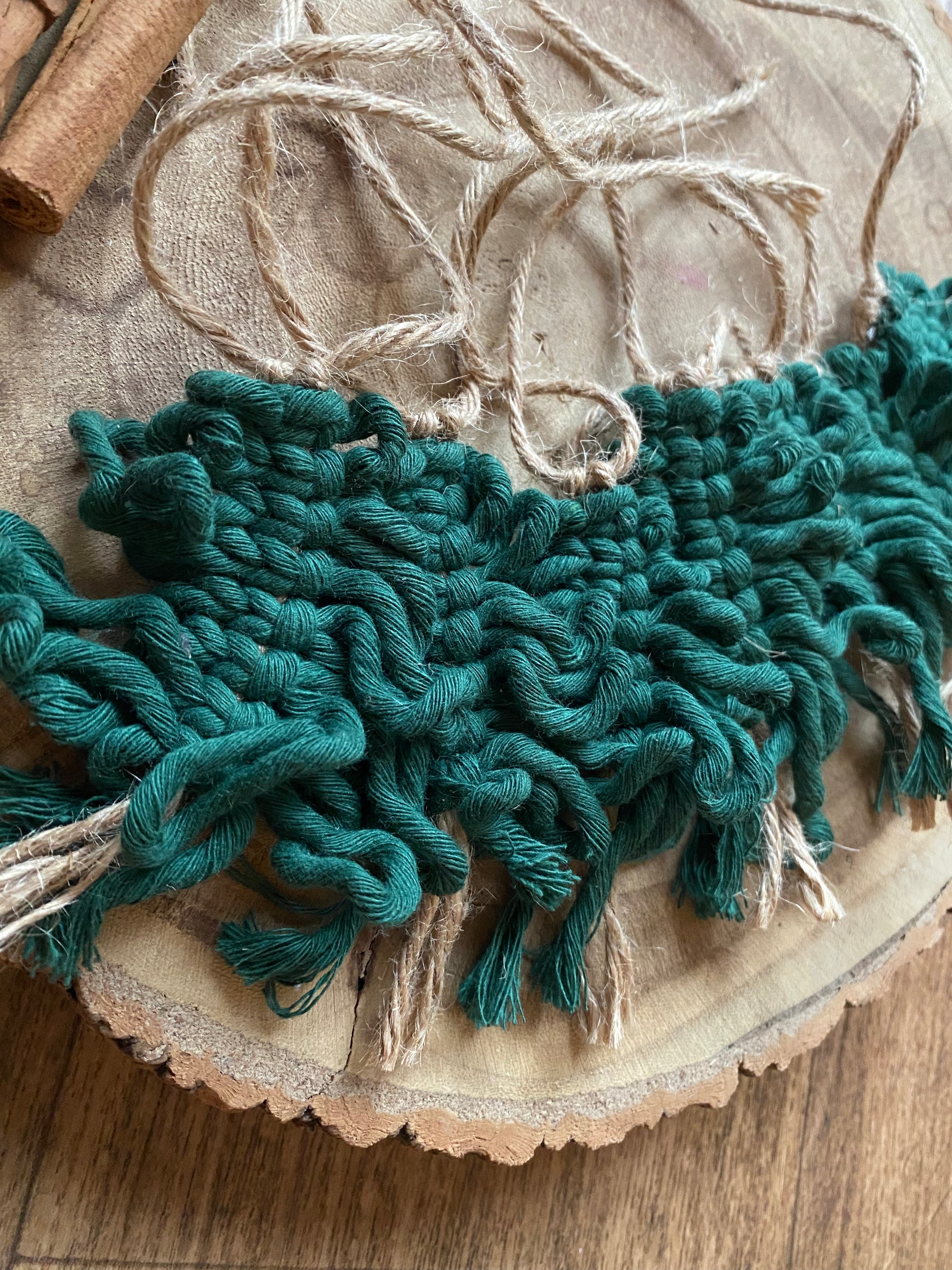 A garland of handmade macrame christmas trees, made with pine green cotton yarn on a length of jute string, displayed neatly on a wooden board.
