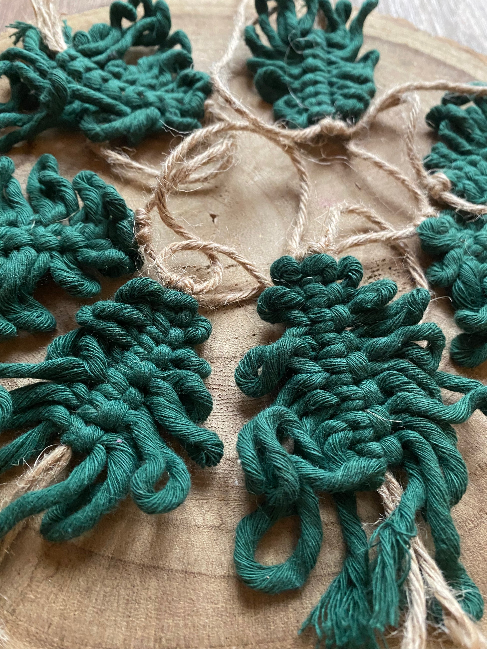 Close up of a garland of handmade macrame christmas trees, made with pine green cotton yarn on a length of jute string, displayed in a circle on a wooden board.
