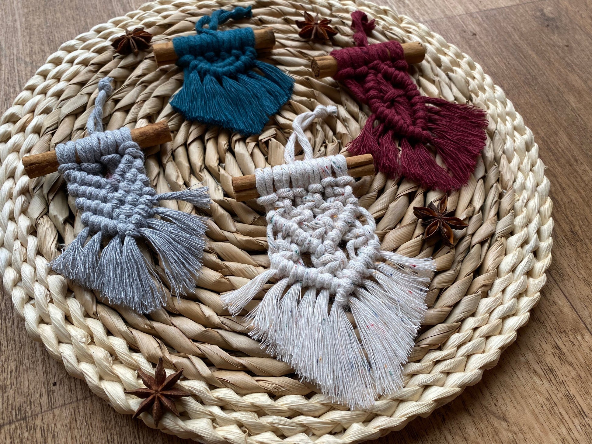 Four handmade macrame christmas tree decorations made with recycled cotton and a real cinnamon stick, laid out on a round wicker mat surrounded by star anise for decoration.