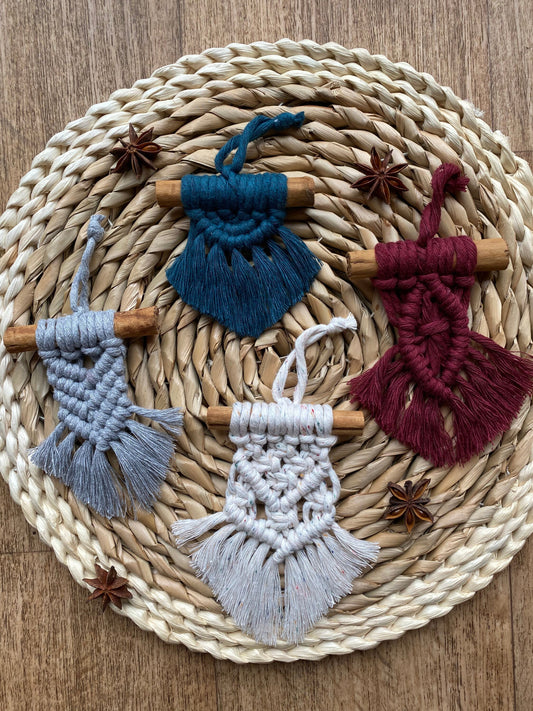 Four handmade macrame christmas tree decorations made with recycled cotton and real cinnamon sticks, laid out on a round wicker mat surrounded by star anise for decoration.