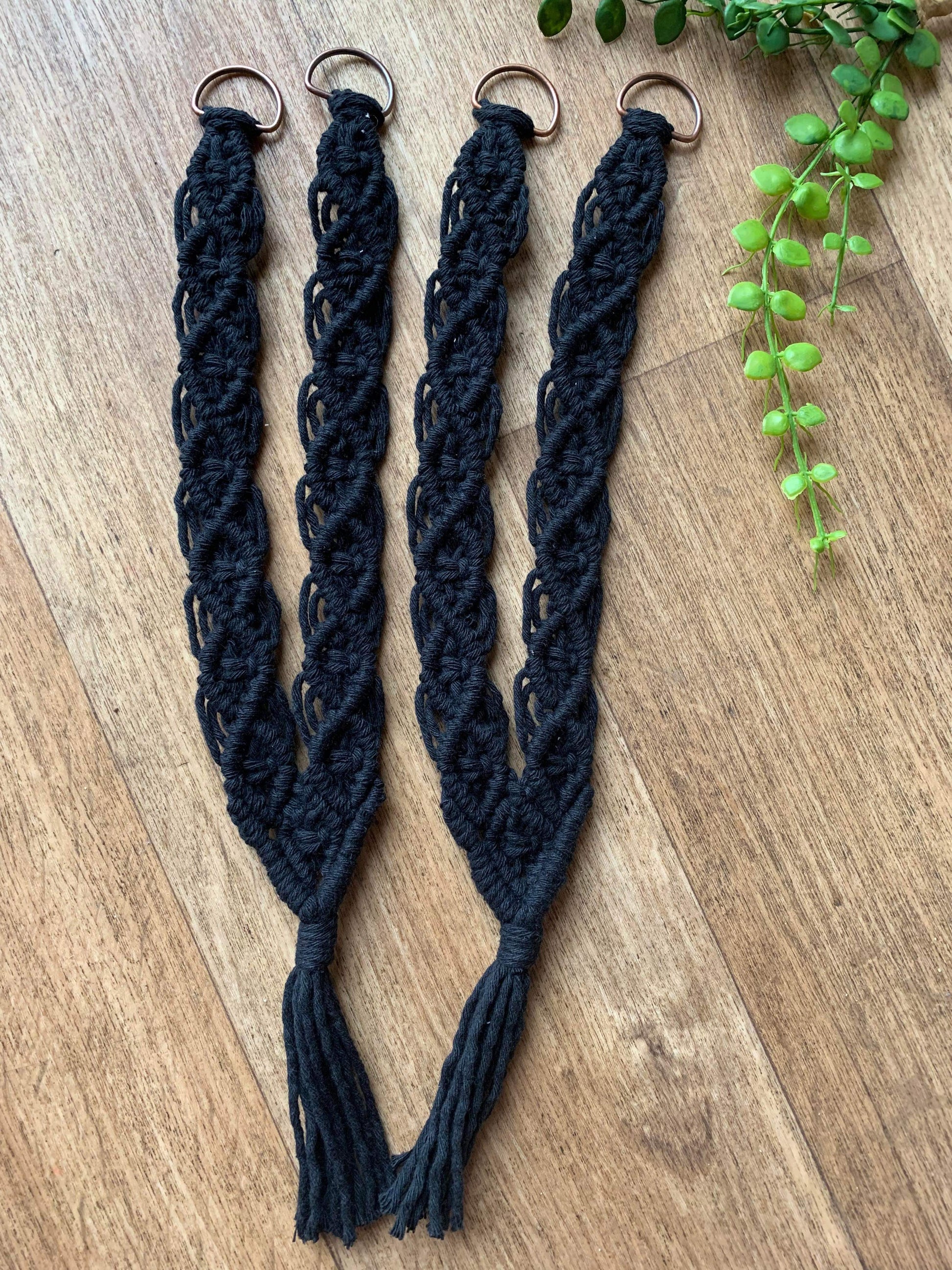 The photo showcases a pair of knotted recycled cotton curtain tie backs intricately woven with back yarn, with metal D rings at one end and tassels at the other end.