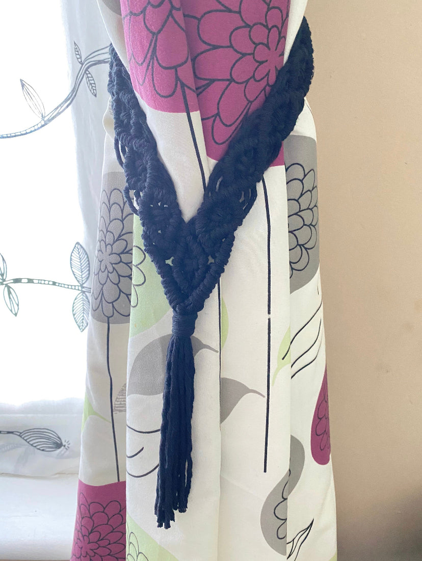 A colourful patterned curtain is neatly held back with a handmade black cotton tie back which has an intricately knotted diamond pattern and long tassel to finish.