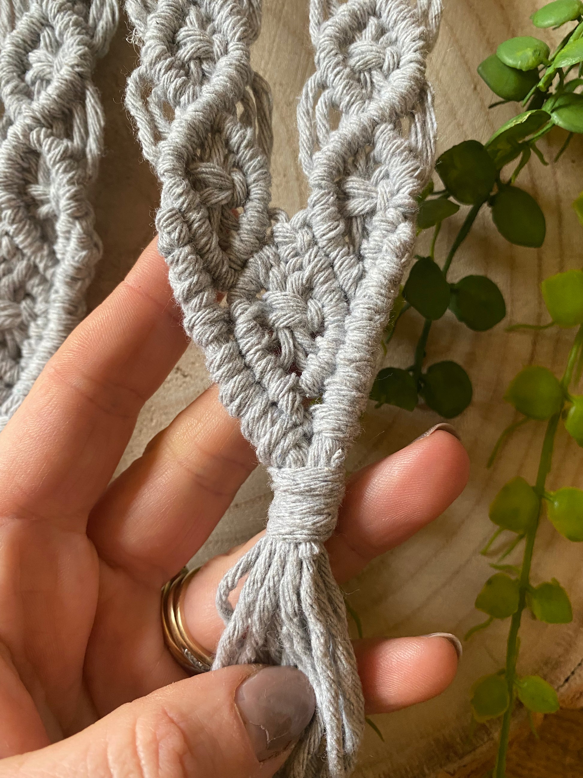 A hand holding the tasseled end of a pair of knotted recycled cotton curtain tie backs made with light grey yarn.