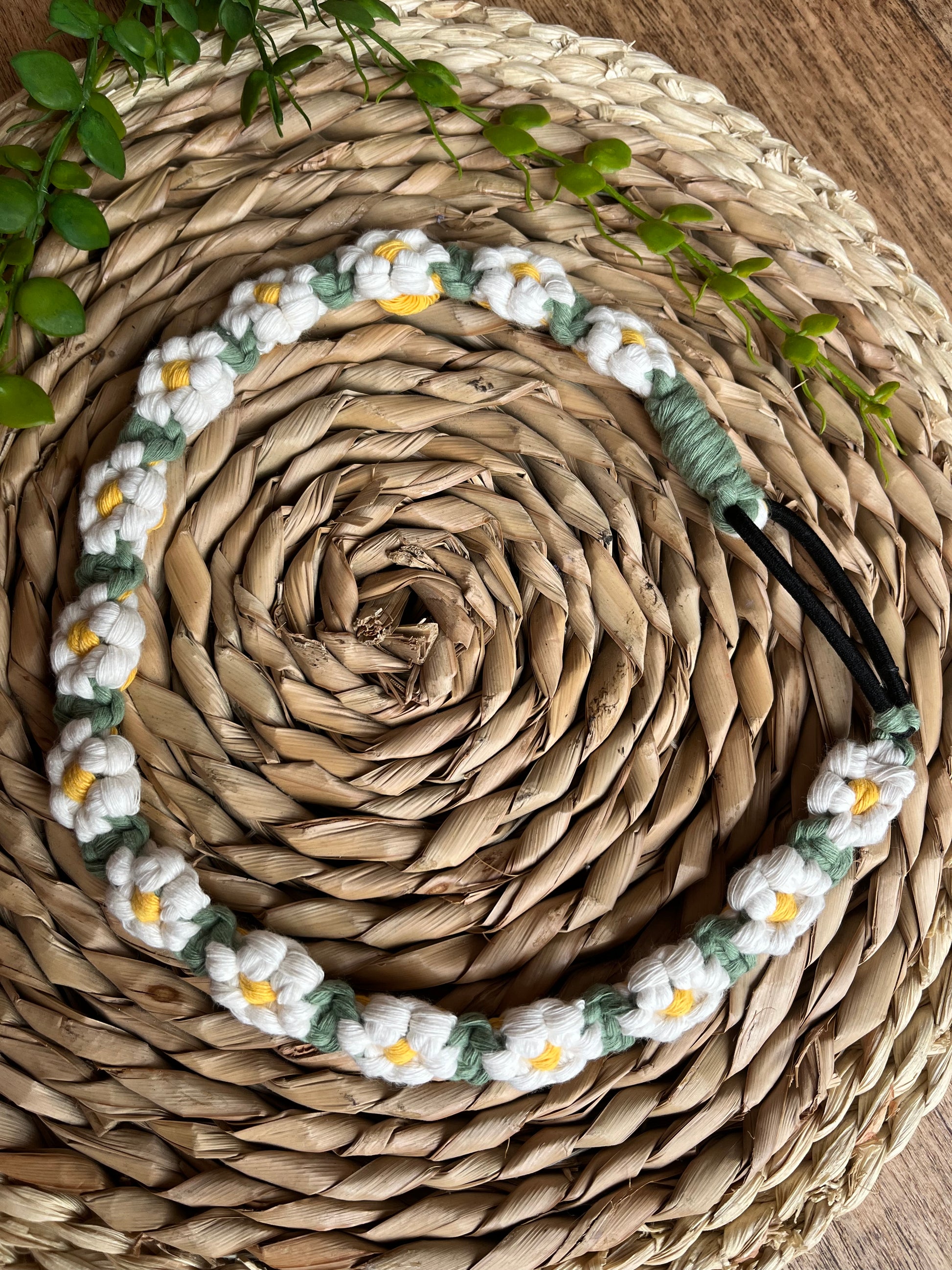 A macrame daisy chain headband made with white yellow and green cotton, laid neatly on a woven placemat.