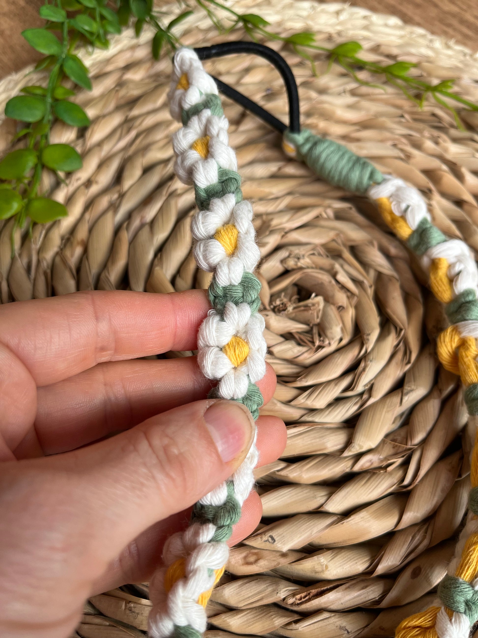 A hand holding a macrame daisy chain headband made with white yellow and green cotton.