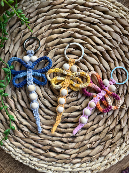 Three handmade macrame dragonfly keyrings made using shades of blue, yellow and pink recycled cotton, on a metal split ring, with small wooden beads.