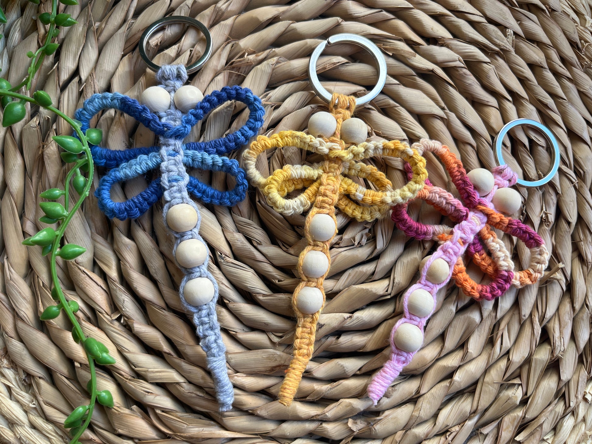 Three handmade macrame dragonfly keyrings, made using shades of blue, yellow and pink recycled cotton, on a metal split ring, with small wooden beads.