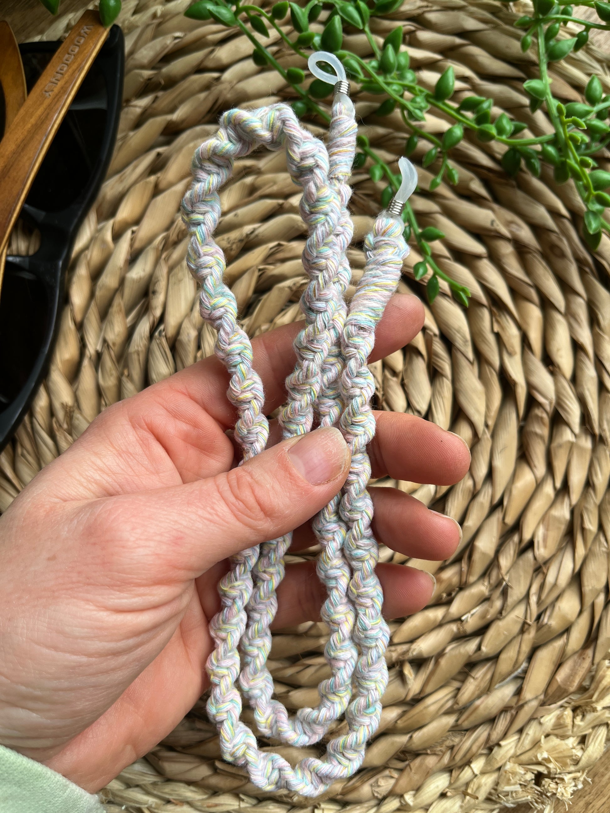 A hand is holding a handmade macrame eyewear holder chain, made with recycled cotton yarn.