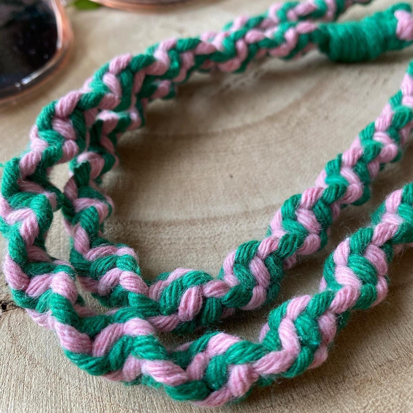 A close up view of a handmade macrame eyewear holder chain, made with pink and green recycled cotton yarn.