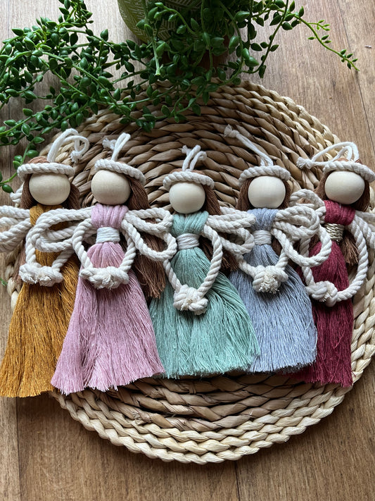 5 macrame fairy dolls laid flat next to each other on a wicker surface. Made with recycled cotton yarn in various colours.
