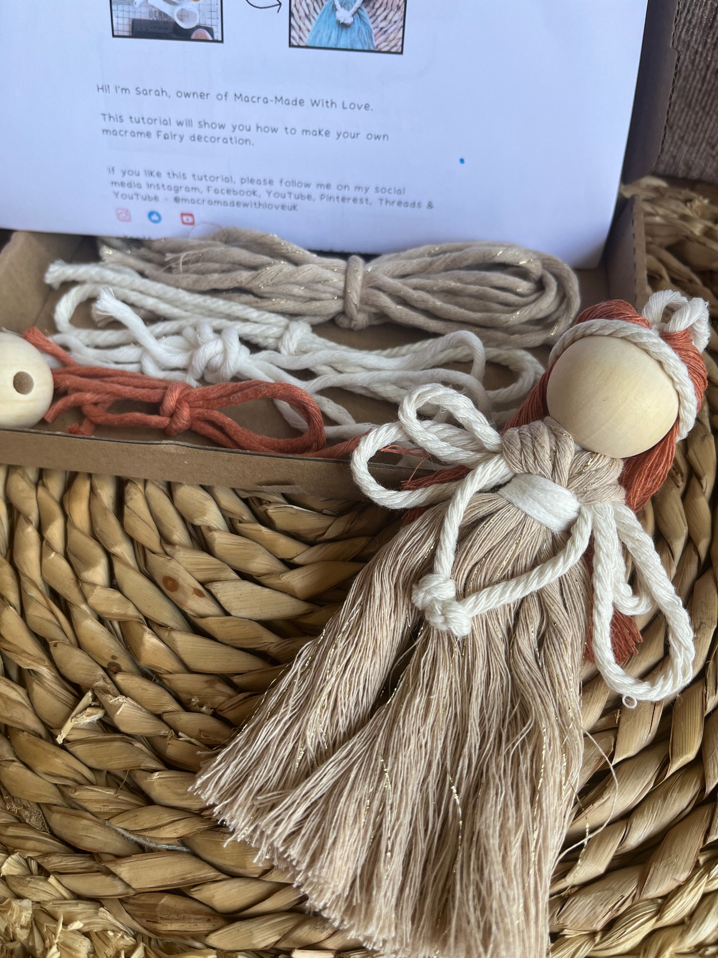 A macrame fairy lays on a wicker mat with a diy craft kit and instructions in the background.