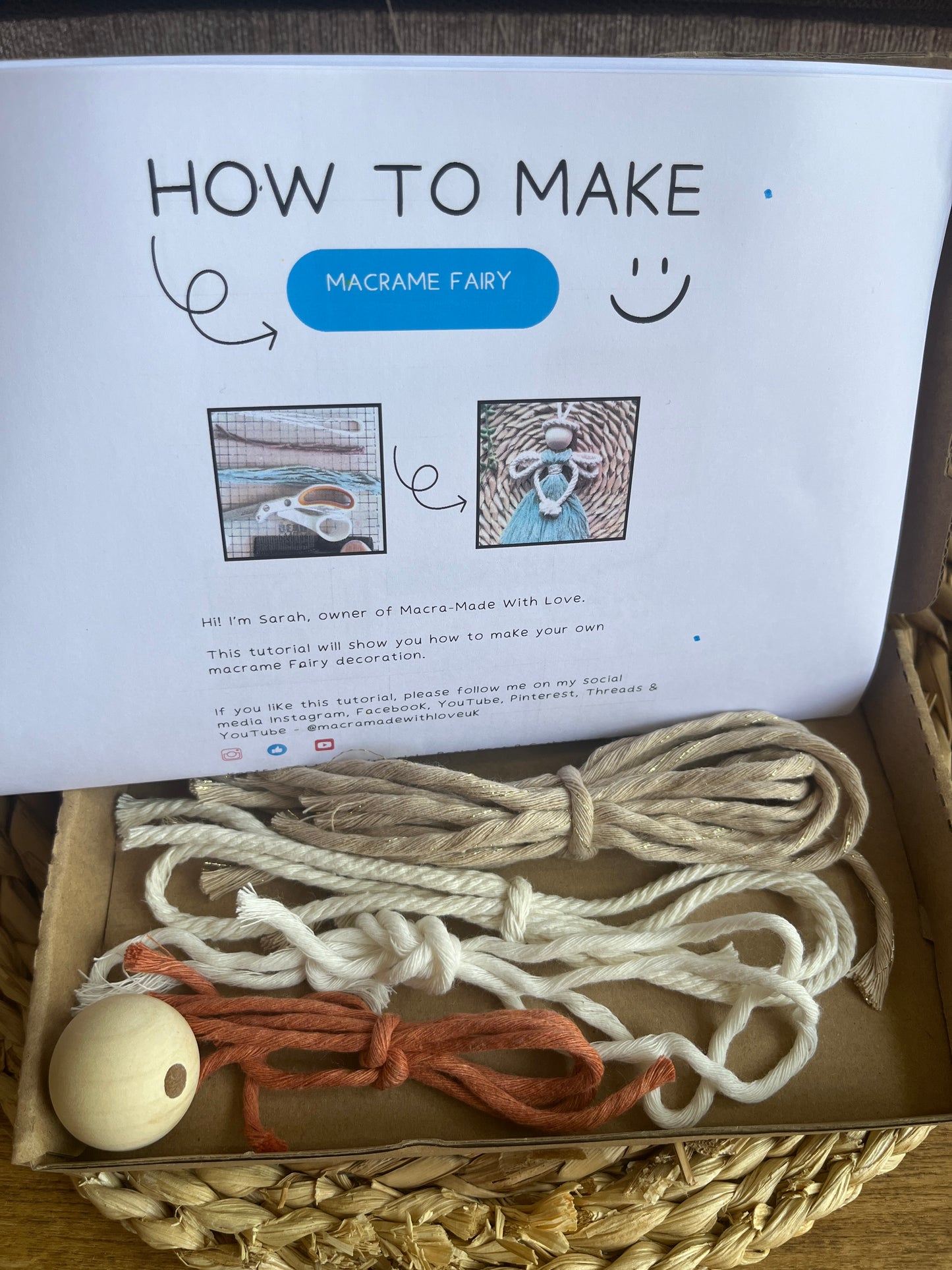 Open box with printed instructions titled 'How to Make Macrame Fairy' with macrame materials inside the box on a wicker surface