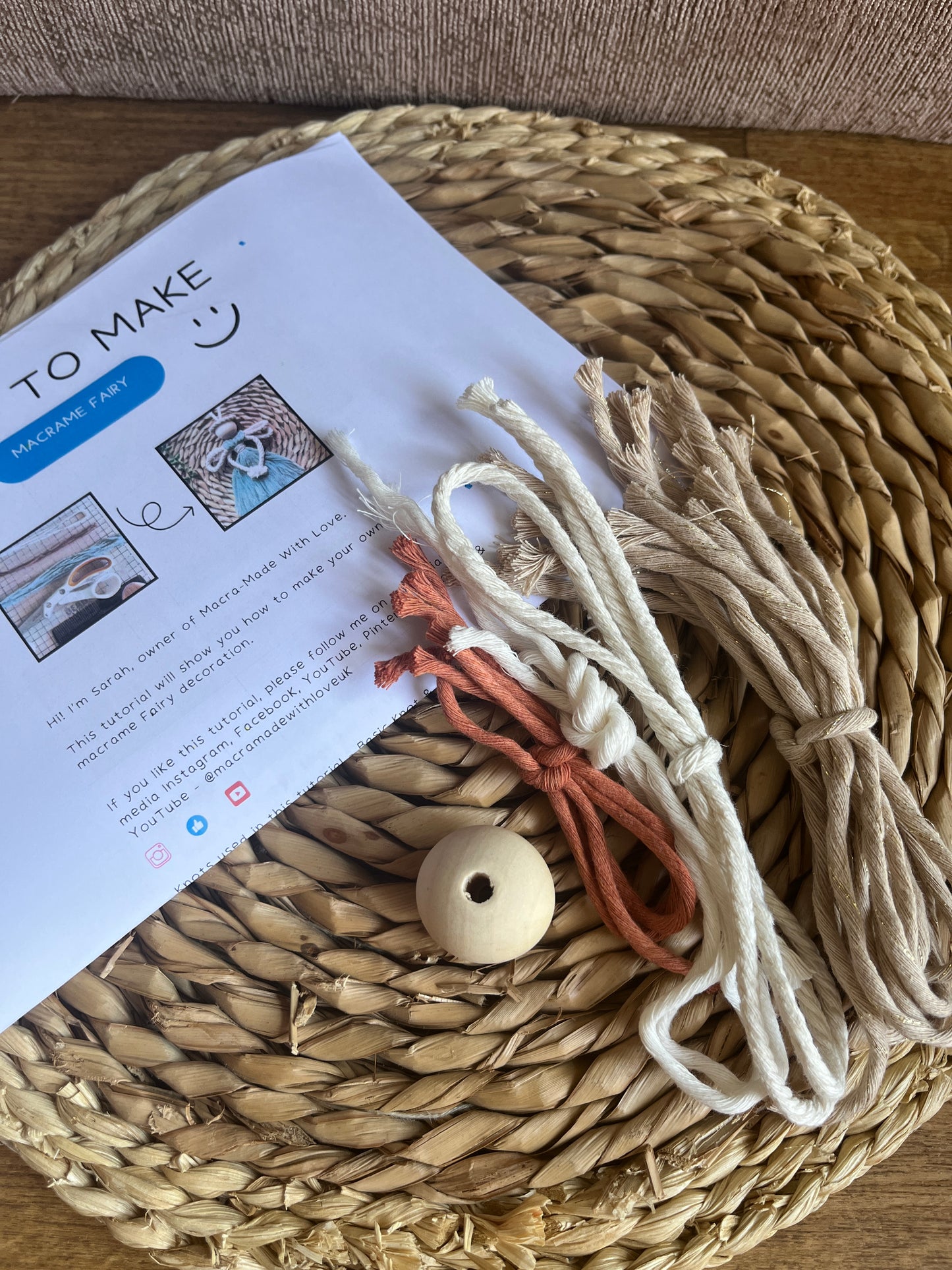 Macrame yarn and a wooden bead next to printed DIY craft kit instructions on a wicker mat.