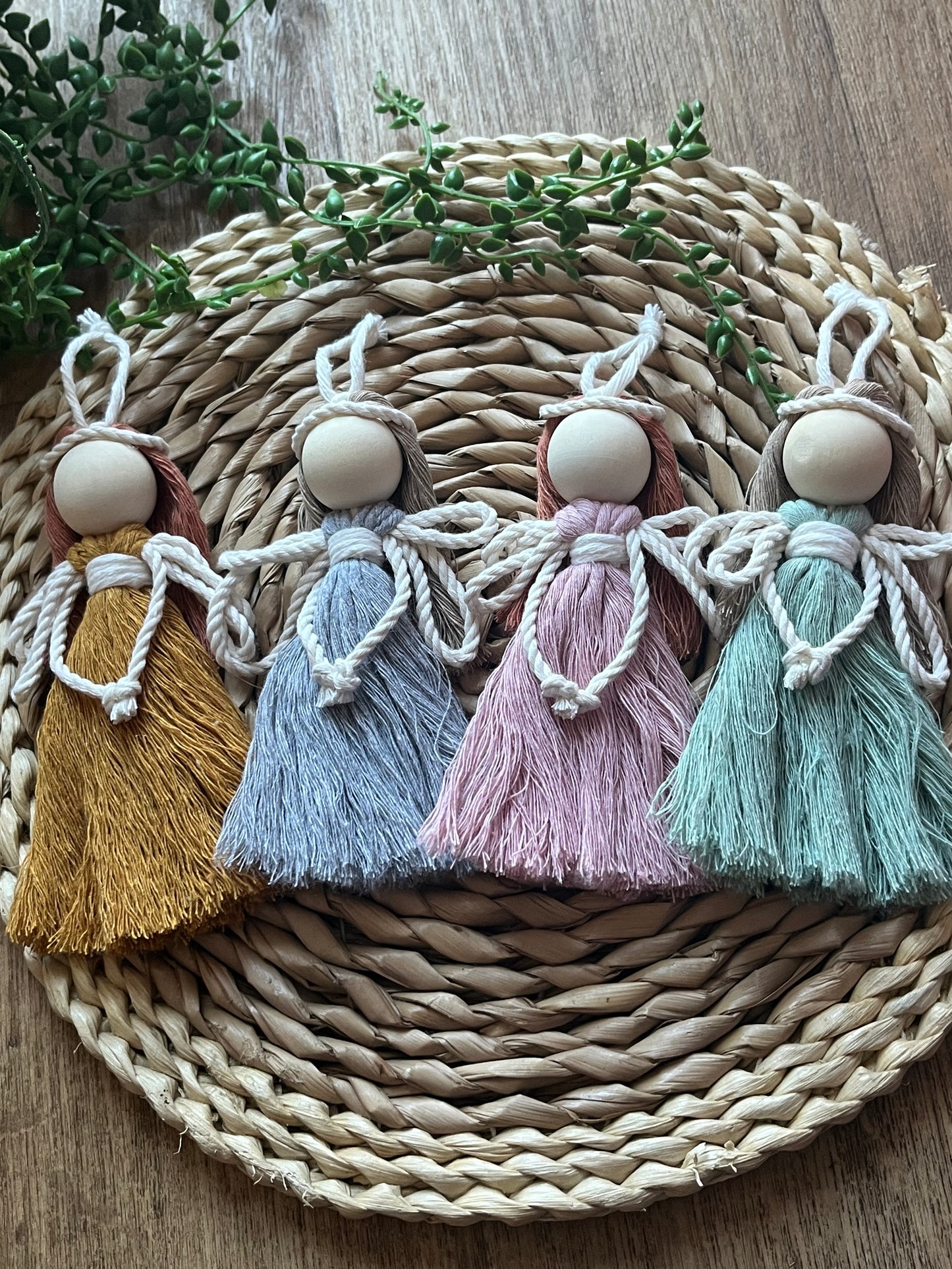 4 handmade macrame fairies with different coloured dresses and hair, laid neatly next to each other on a woven wicker surface.