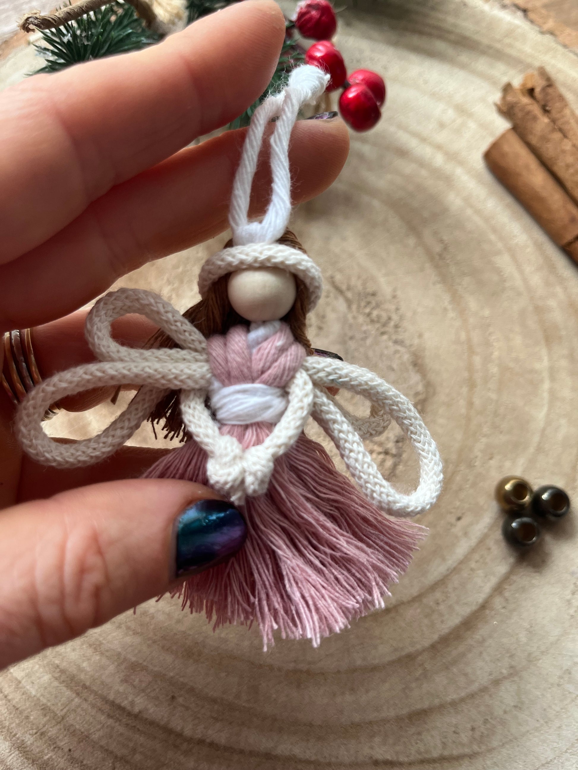 Close up of a hand holding a handcrafted macrame fairy ornament with knotted wings and blush pink dress.