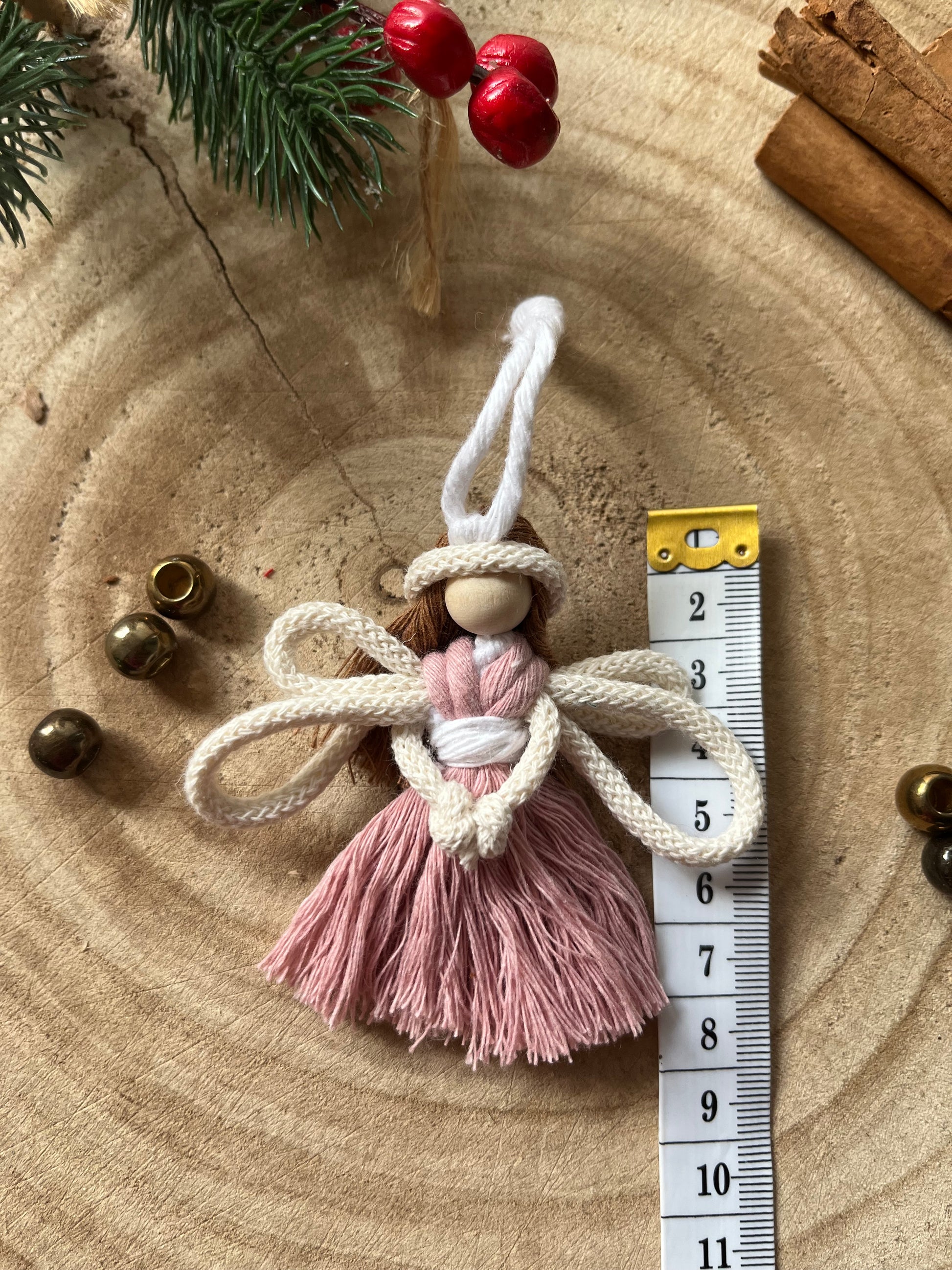 8cm handmade macrame fairy Christmas tree decoration in blush pink cotton, shown next to a white tape measure on a wooden surface.