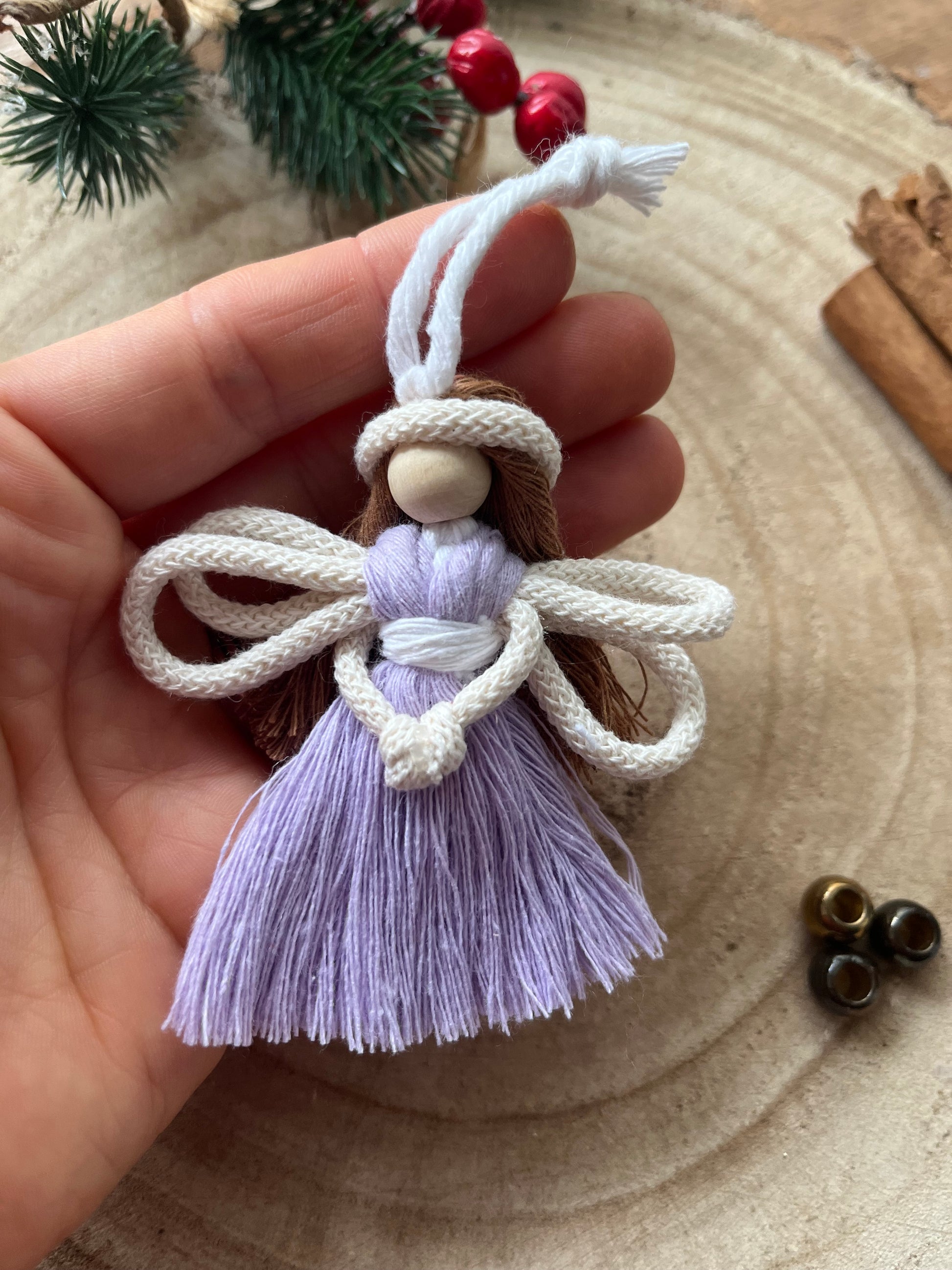 Close up of a hand holding a handcrafted macrame fairy with knotted wings and lilac dress.