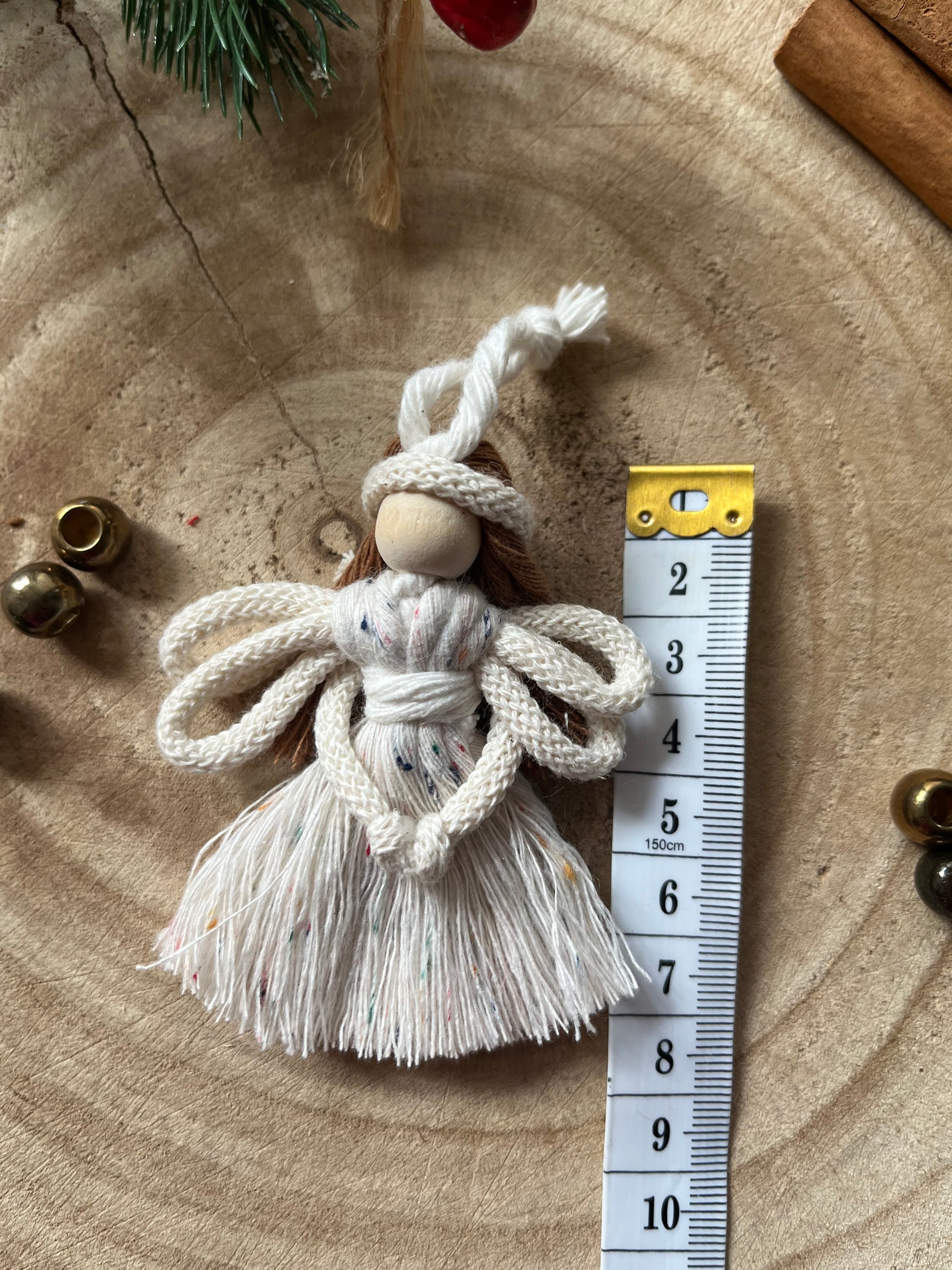 8cm handmade macrame fairy Christmas tree decoration in natural cotton, shown next to a white tape measure on a wooden surface.