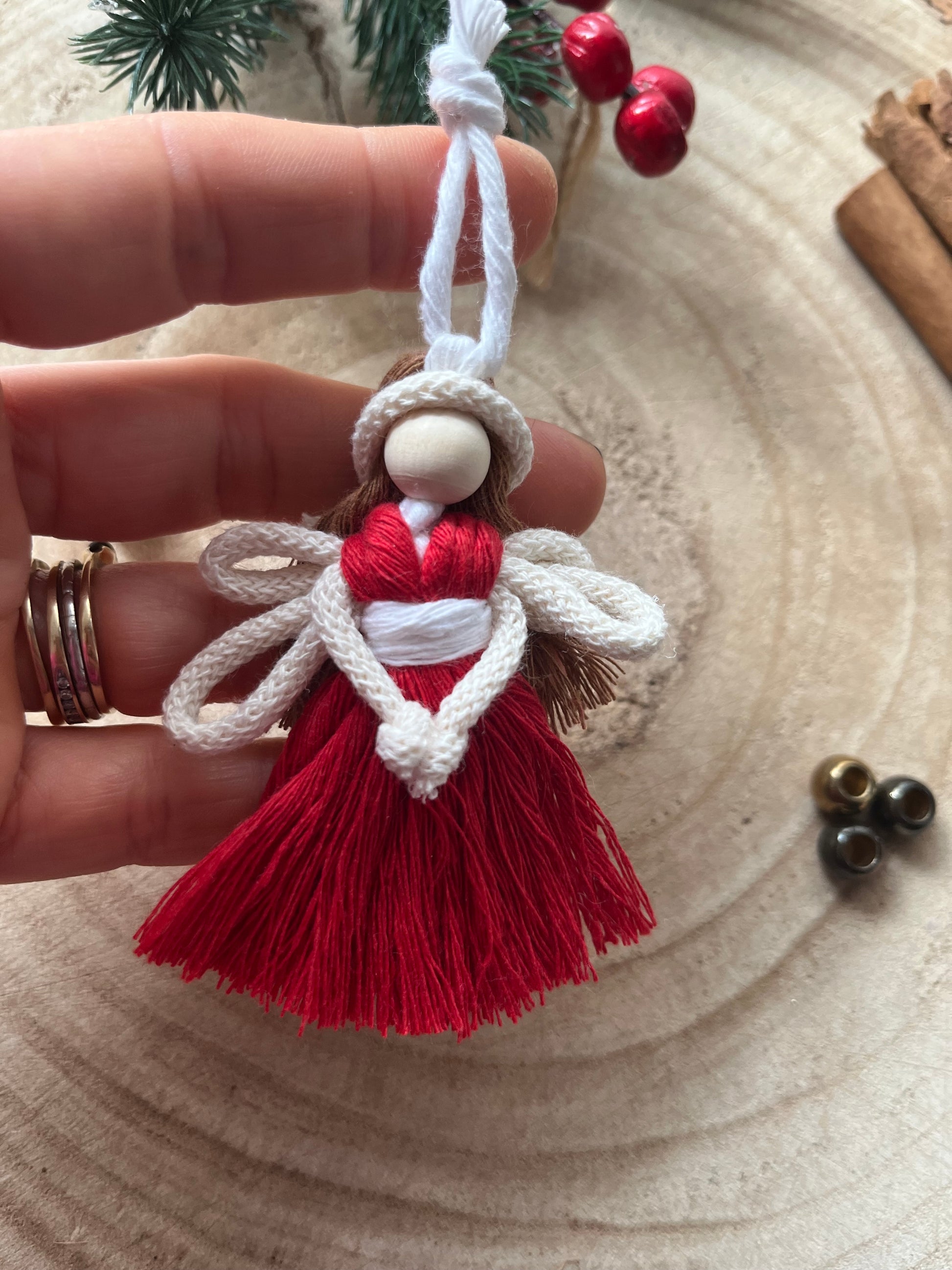 Close up of a hand holding a handcrafted macrame fairy ornament with knotted wings and red cotton dress.