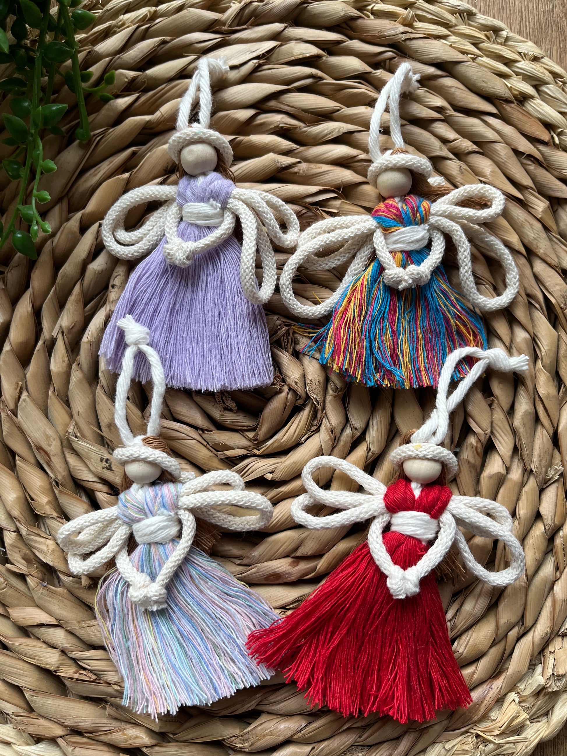 Four 8cm handmade macrame fairy Christmas tree decorations in a variety of colours, on a wicker surface.