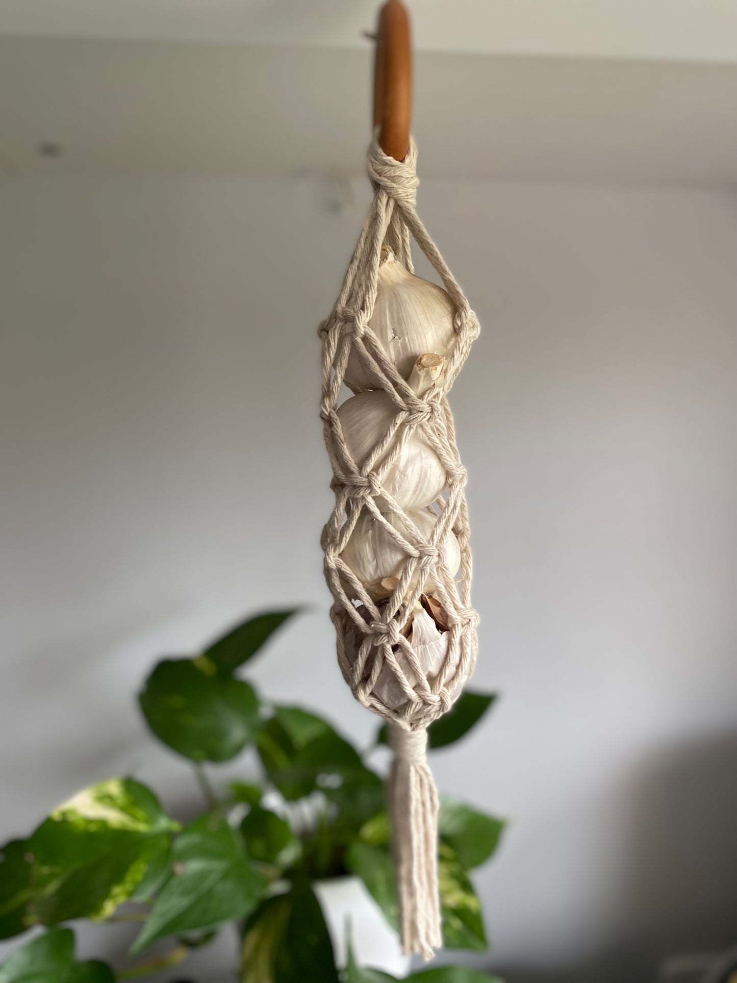 A handmade macrame garlic hanger made with natural cotton yarn and a wooden ring, with 4 fresh garlic bulbs inside.