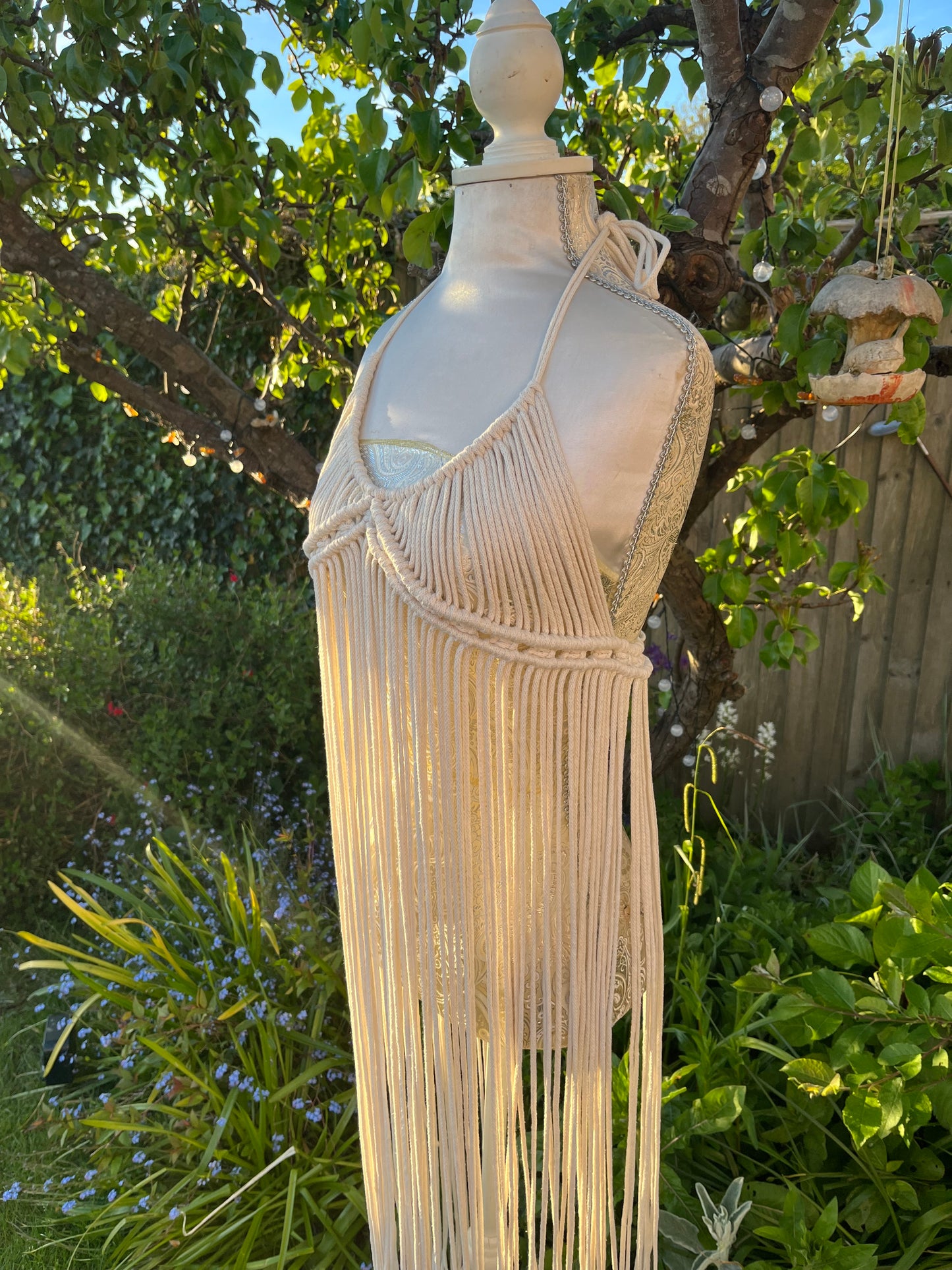 A beige, one-size macrame boho goddess dress with halter neck, displayed on a mannequin outdoors.