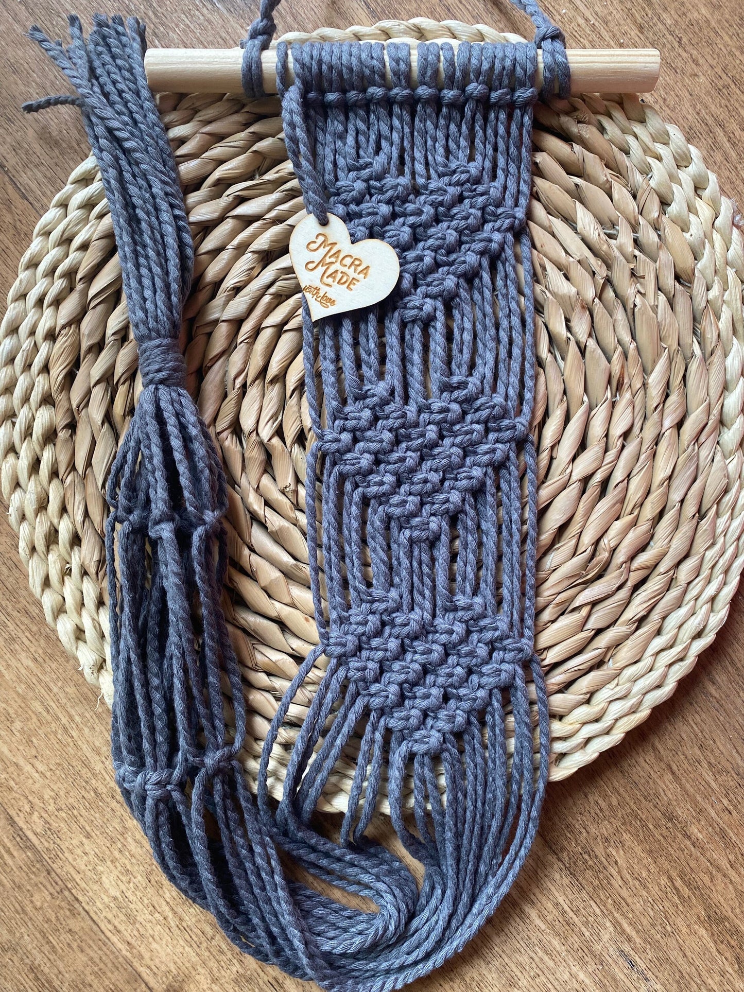 A wall hanging macrame plant hanger in grey yarn, laid neatly on a round wicker mat.