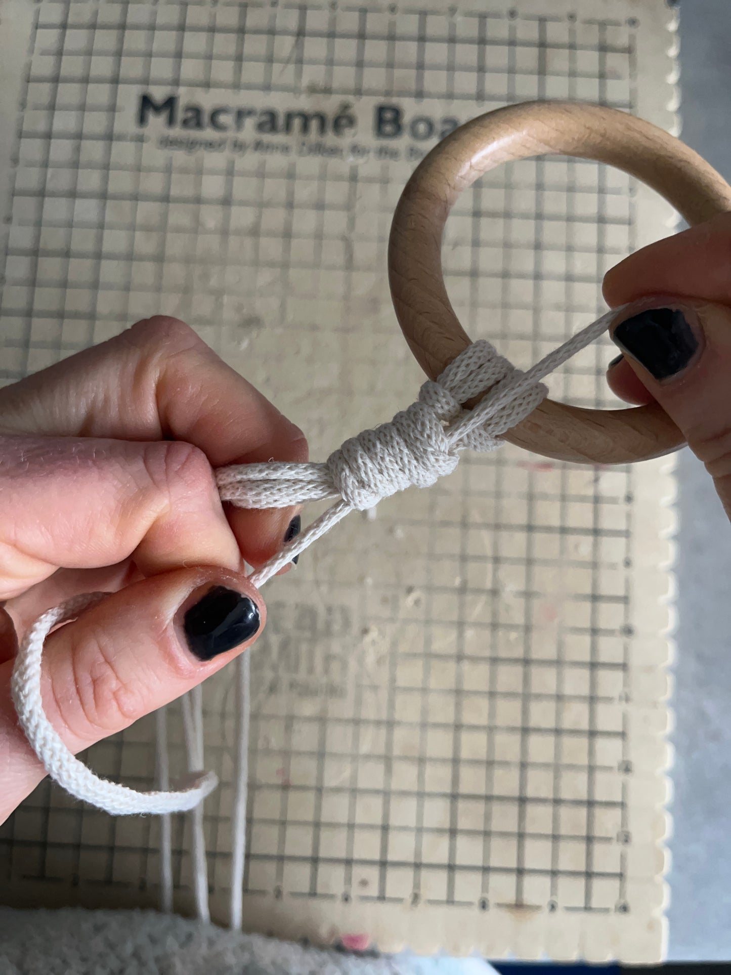A persons hands pulling on white yarn attached to a wooden ring