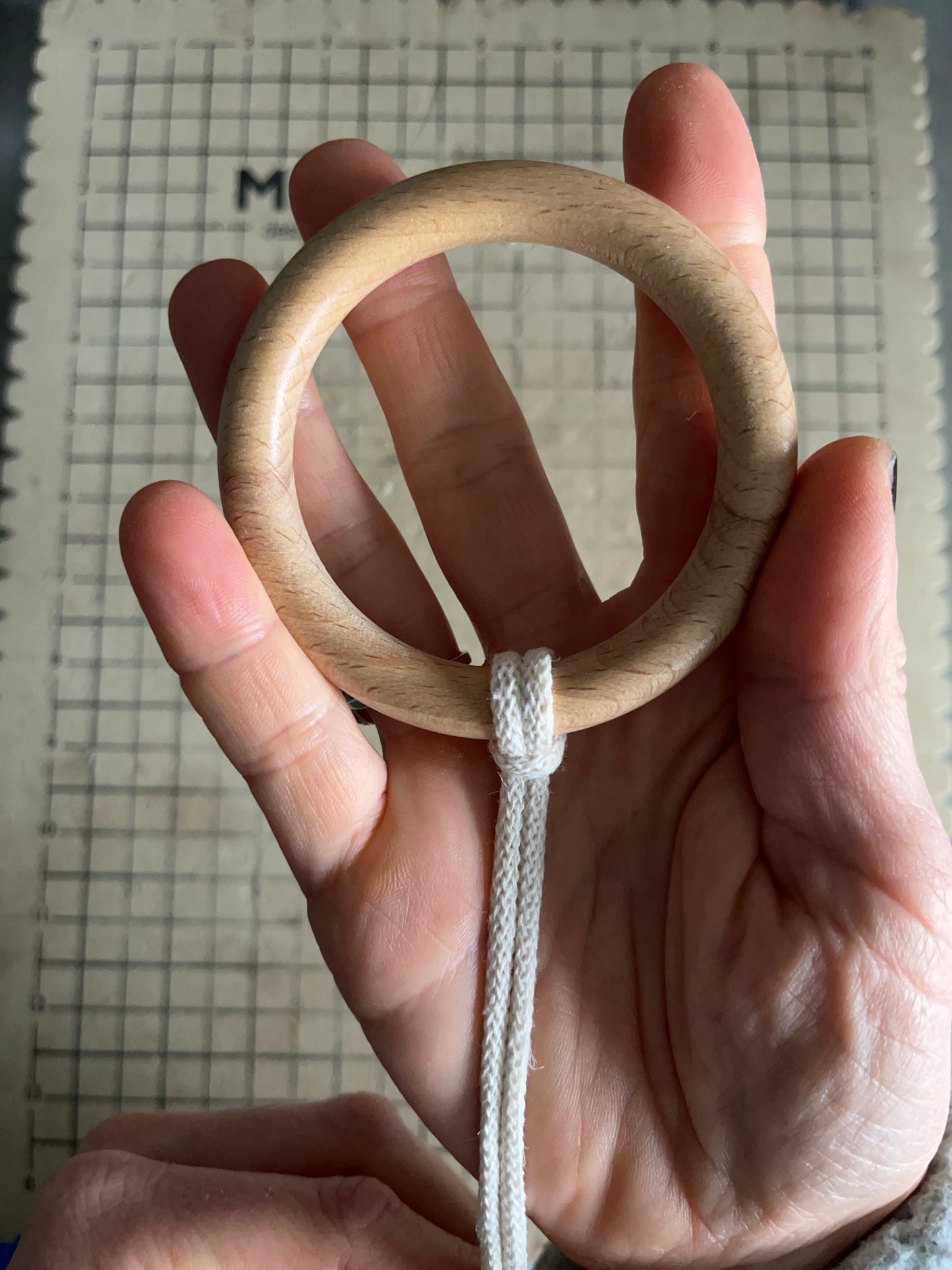 A hang holding a large wooden ring with natural yarn attached to it