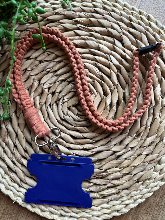 A handmade macrame knotted lanyard, made with recycled cotton in terracotta, with a metal clasp and safety break finish. Shown with a blue ID badge holder attached to it.