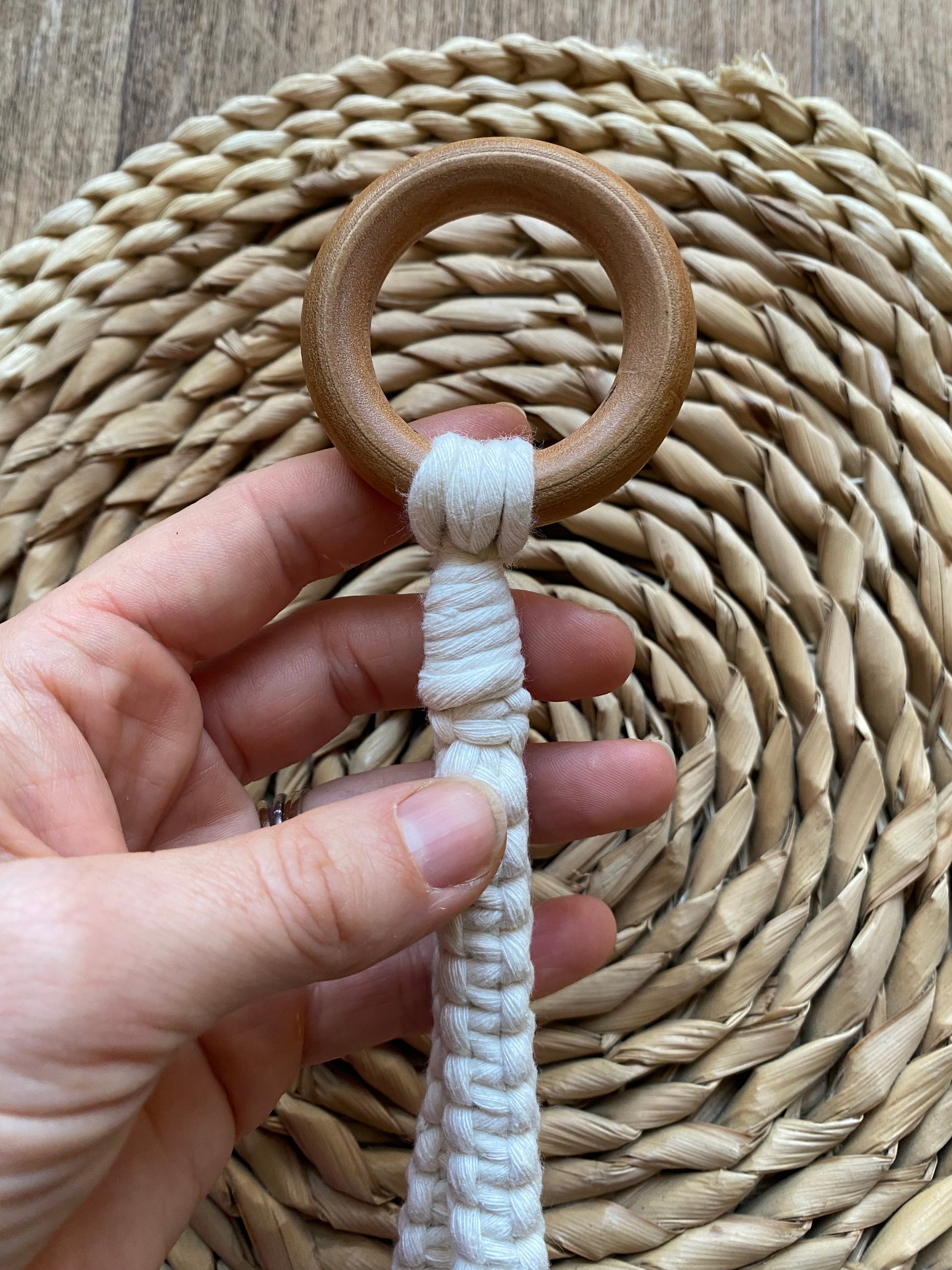 A hand holding the wooden ring at the top of a macramé loop made with natural yarn.