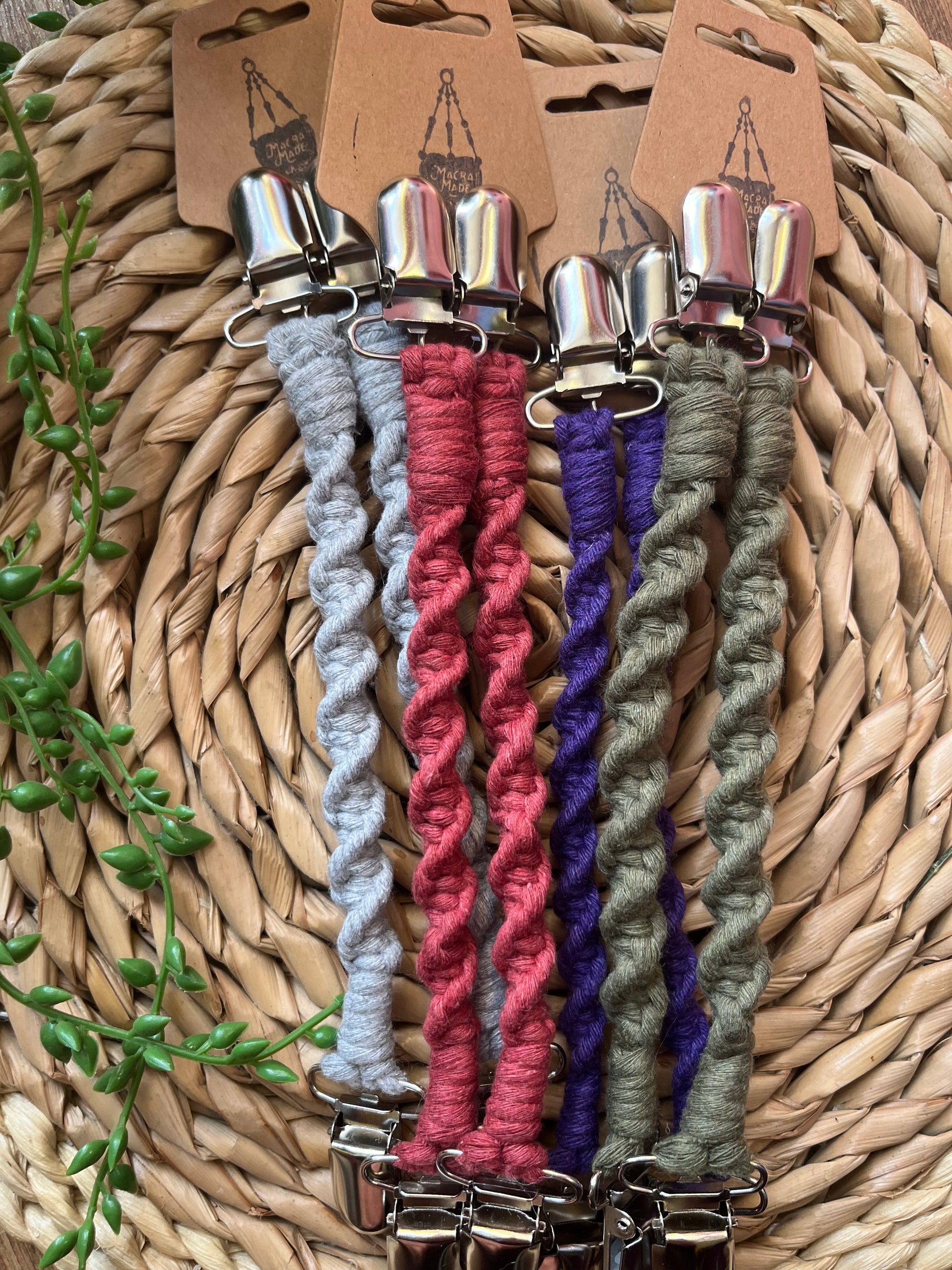 Four pairs of handmade macrame mitten clips made with a twisted knot pattern, with metal clips on each end, attached to cardboard tags.