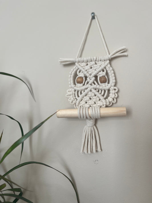 Handmade macrame owl wall hanging decoration, perched on a wooden dowel. Made with recycled cotton and wooden beads.