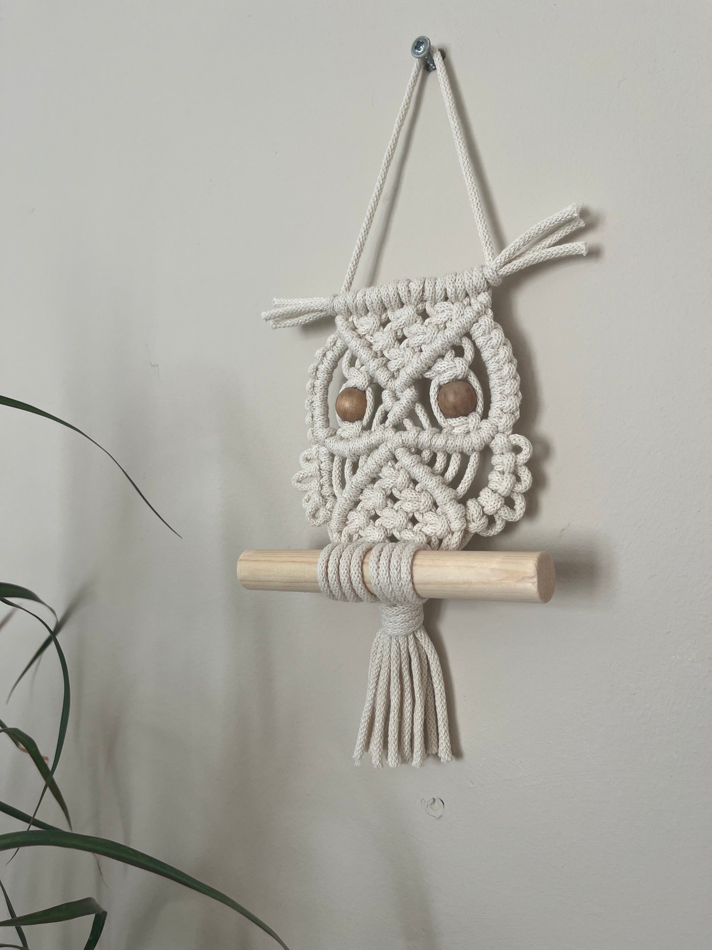 Handmade macrame owl wall hanging decoration, perched on a wooden dowel. Made with natural cotton and wooden beads.
