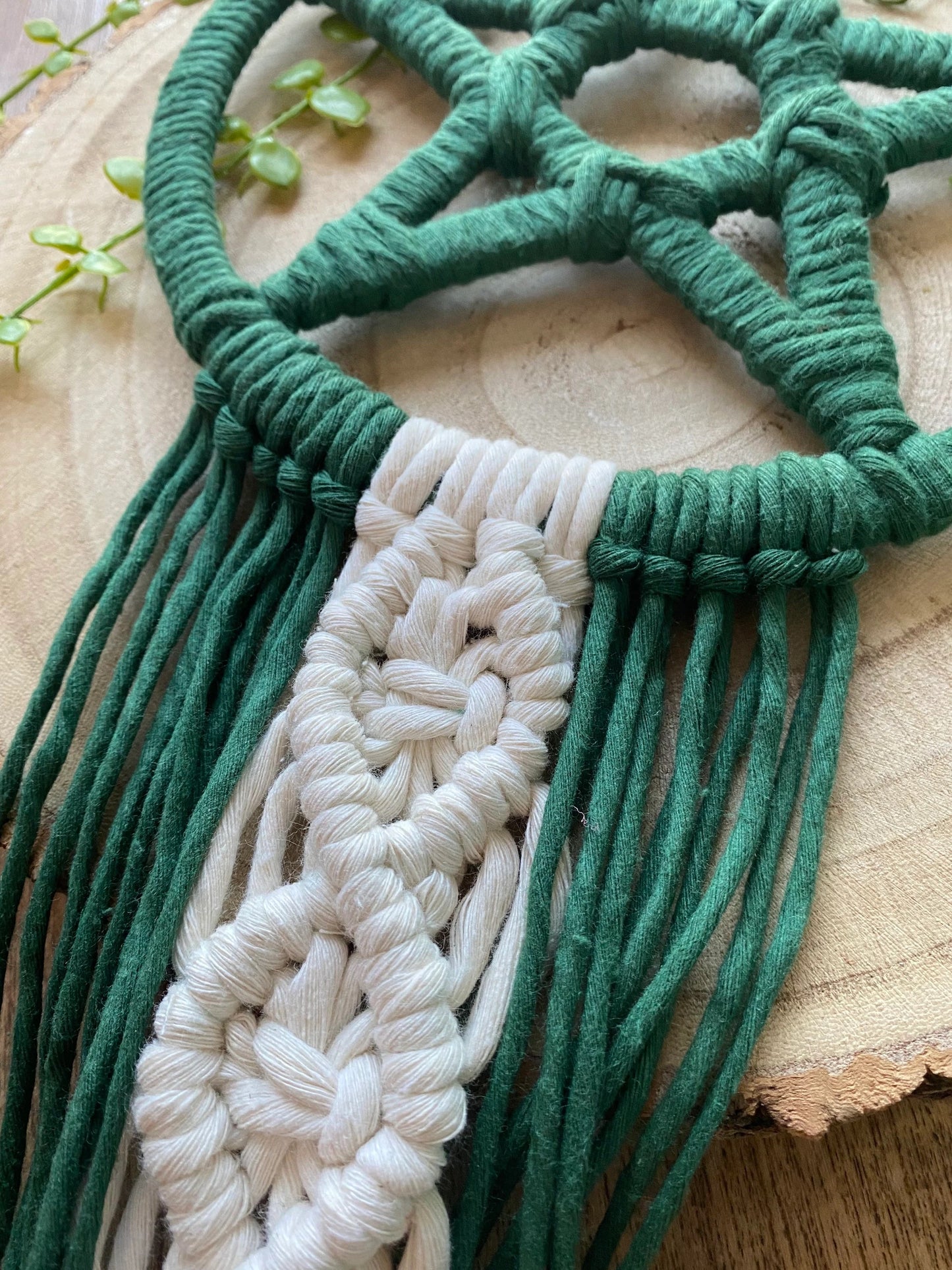 Handmade macrame pentagram wall hanging made with green and natural yarns laid across a wooden surface.